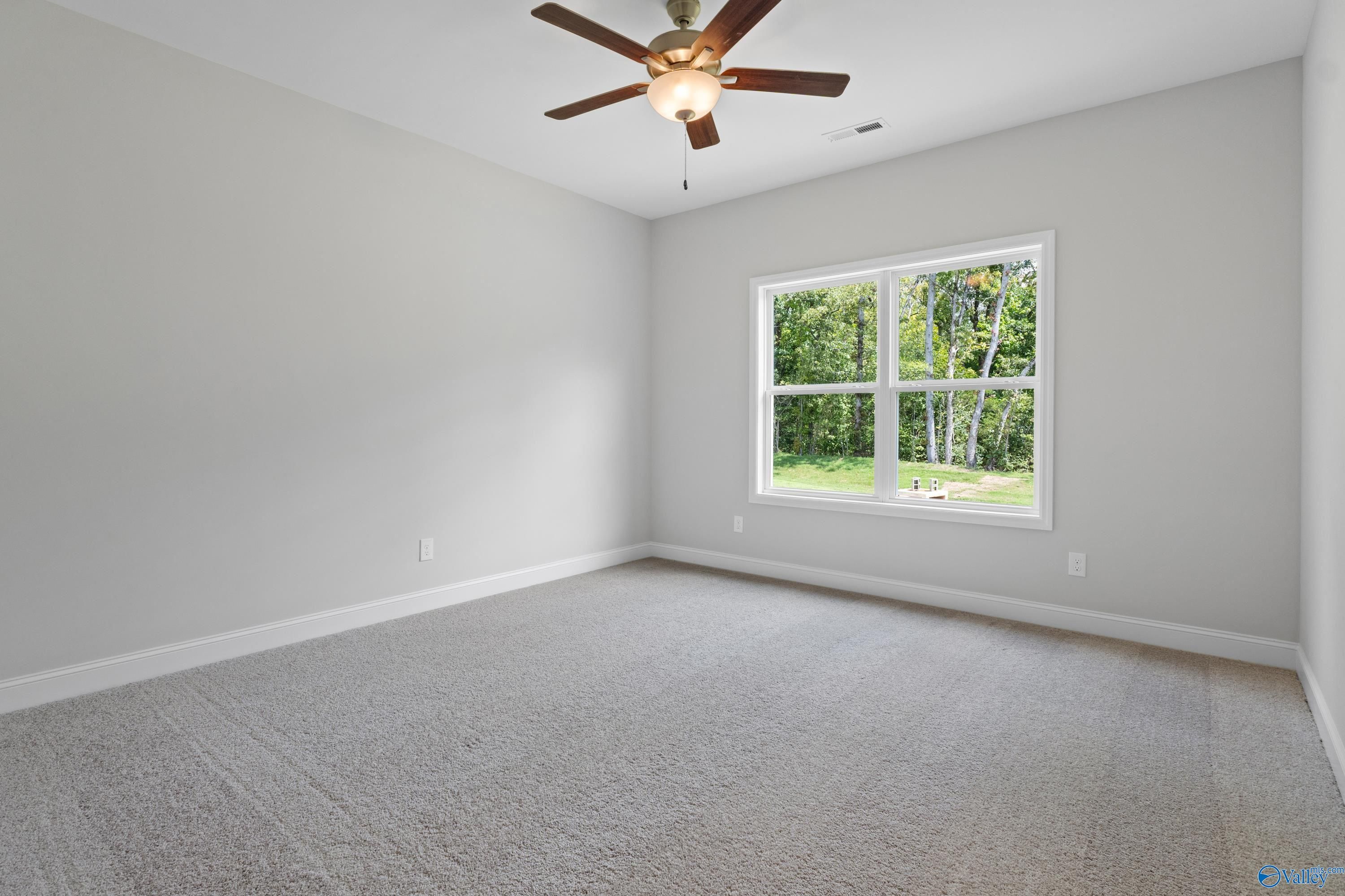 Spacious empty bedroom with ceiling fan, gray walls, carpet floor, and large window overlooking trees in Davidson Homes The Asheville, Huntsville