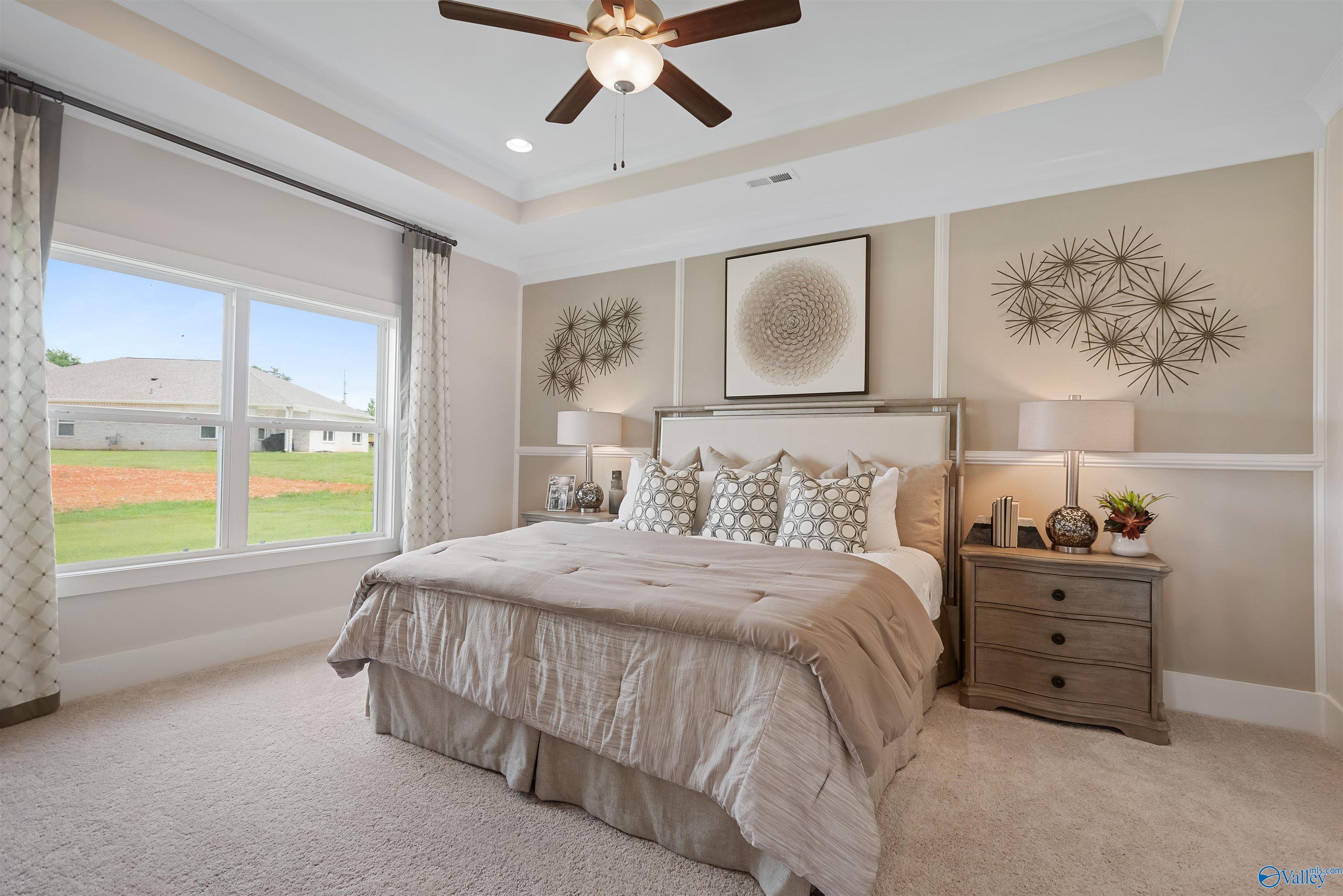Elegant master bedroom with king bed, tray ceiling, ceiling fan, and window views of green fields in Davidson Homes The Everett, New Market, Alabama