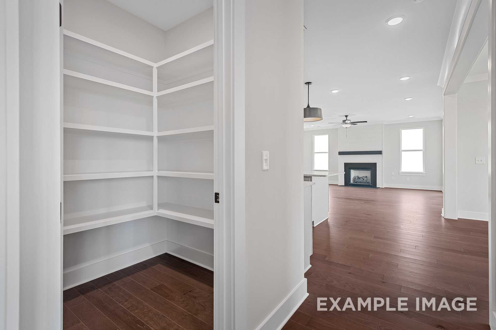 Spacious white corner pantry with shelves in The Hathaway, open to kitchen and great room featuring fireplace, hardwood floors