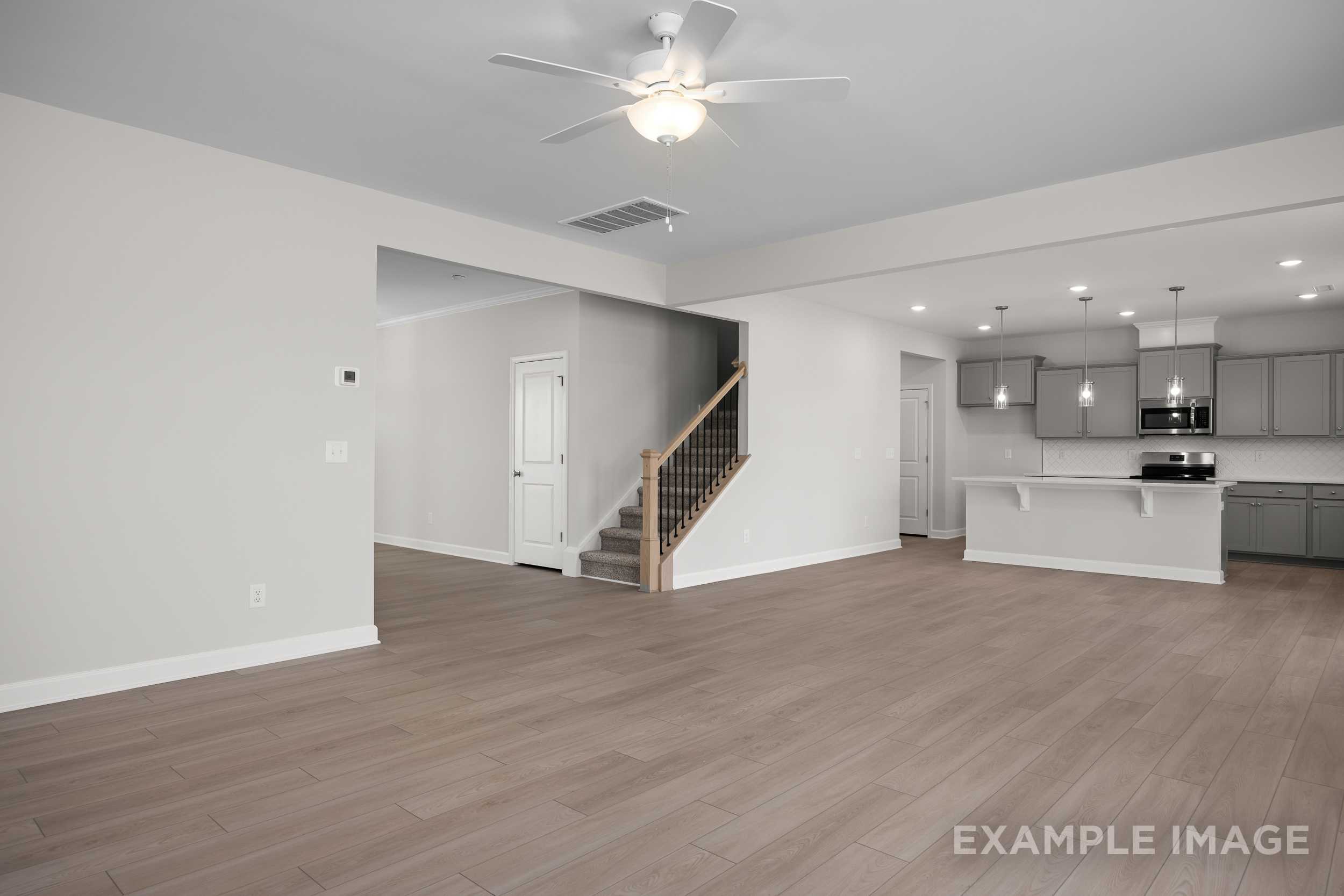 Spacious open-concept interior of The Hickory II showcasing modern kitchen with white cabinets, island, hardwood floors, and staircase