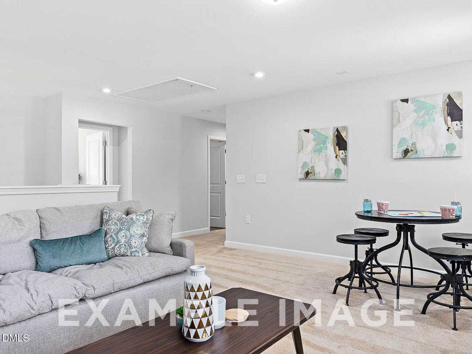 Modern living room with gray sectional sofa, wooden coffee table, and black bar stools in Davidson Homes The Chestnut B, Lillington, NC