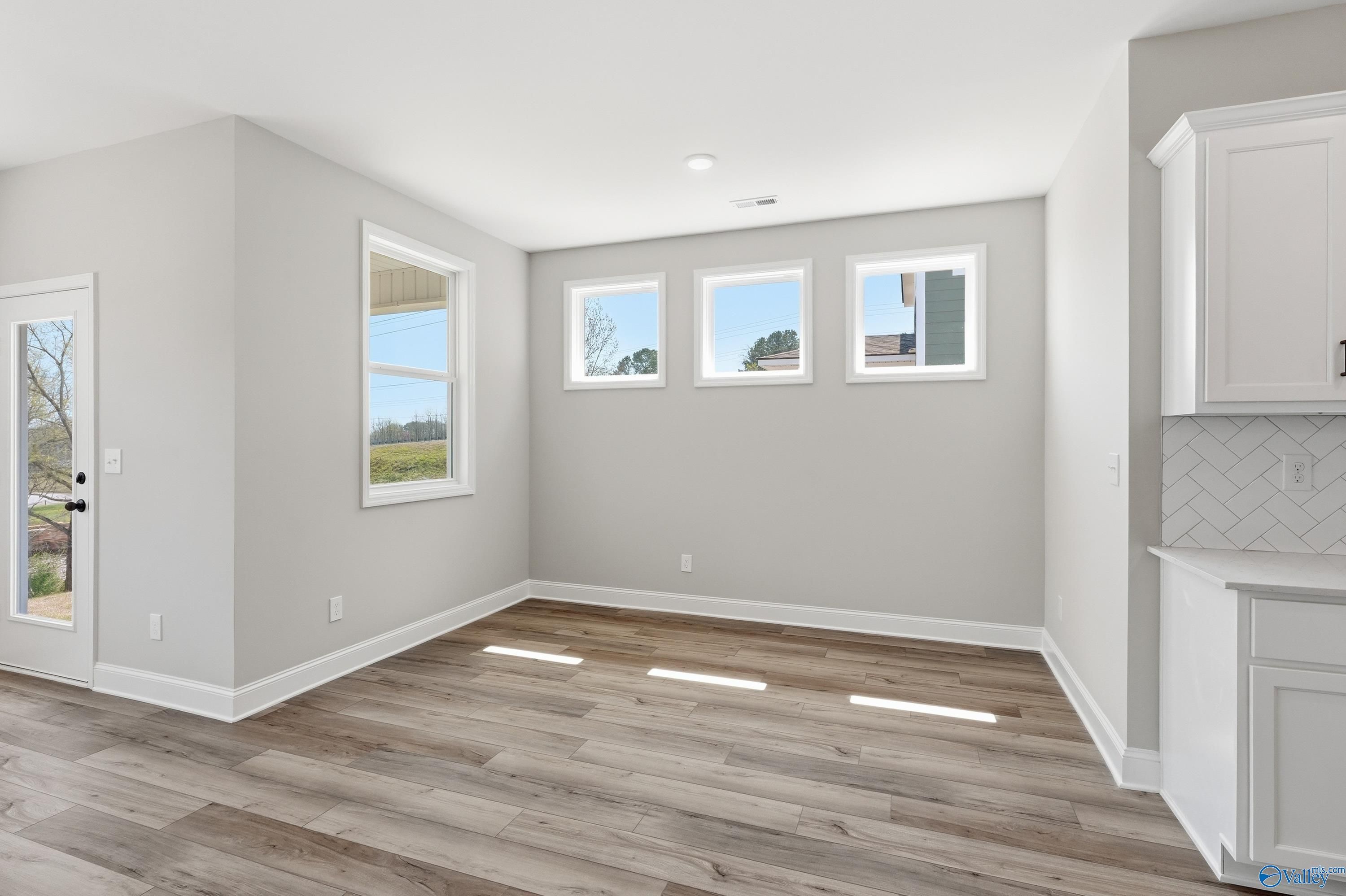 Bright breakfast nook with large windows, gray walls, white cabinets, and luxury vinyl plank floors in Davidson Homes The Laurel K, Cullman, Alabama