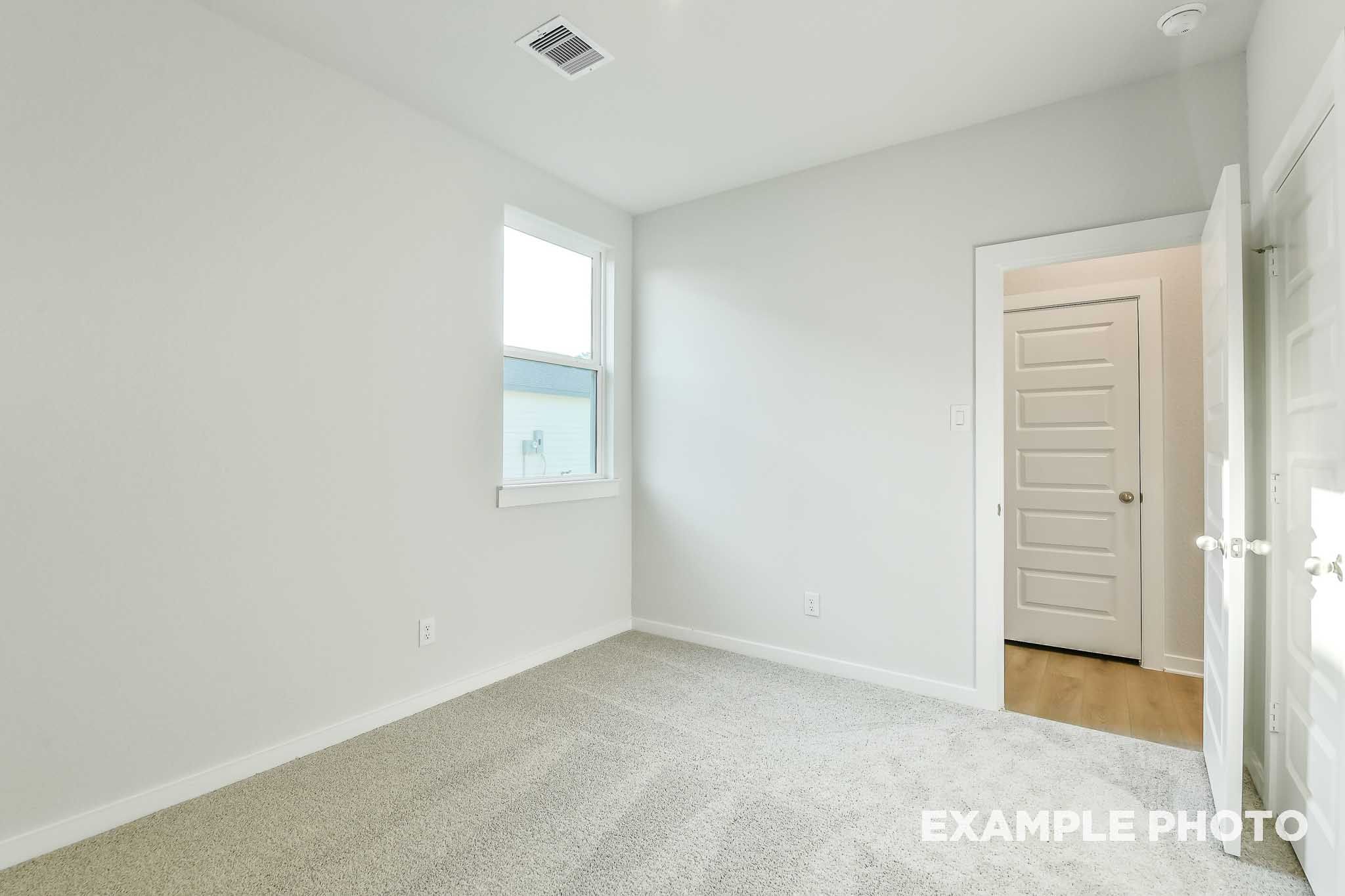 Bright empty bedroom with white walls, carpet flooring, and window in The Colorado by Davidson Homes, Beasley, TX.