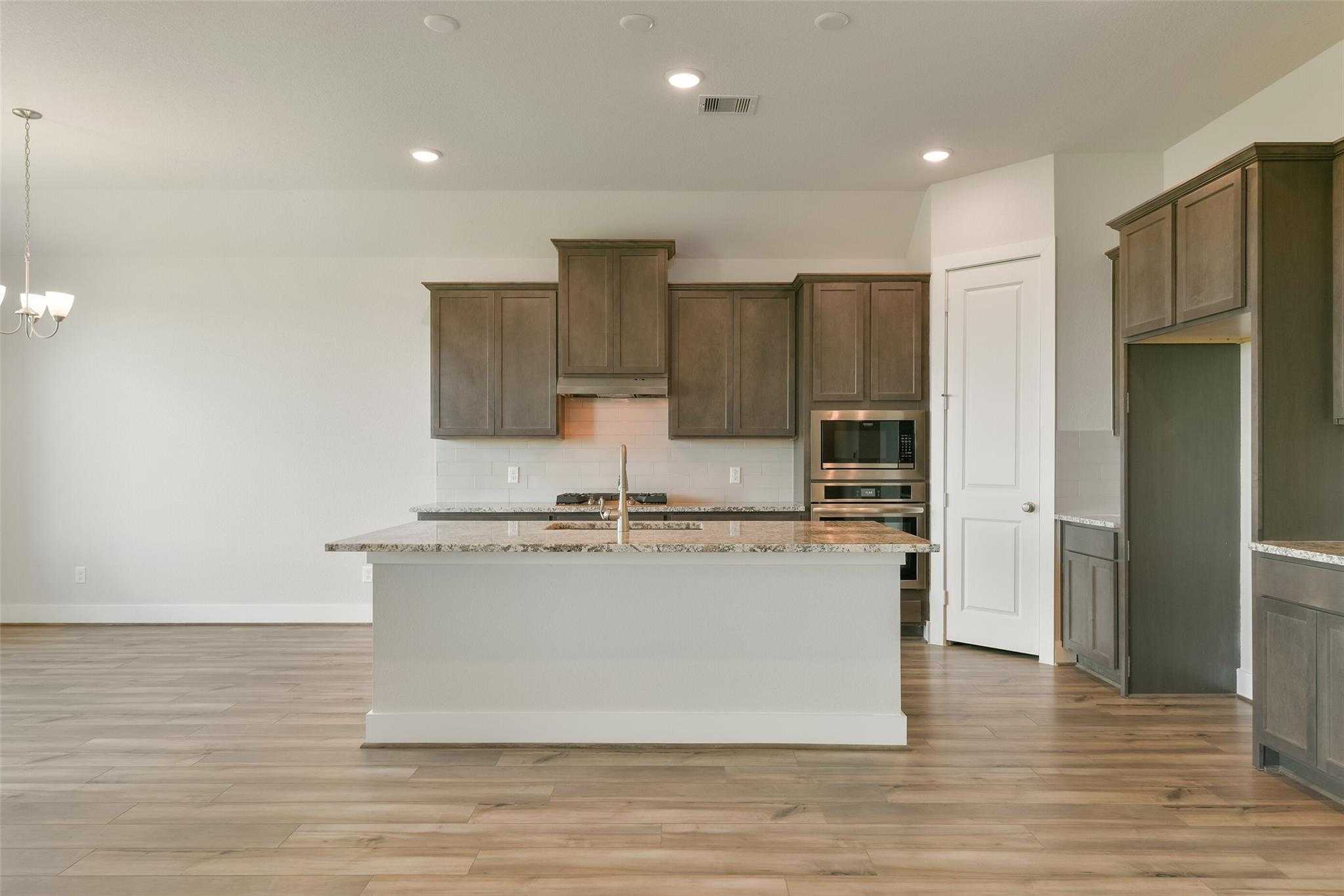 Modern open-concept kitchen with large granite island, shaker cabinets, stainless appliances in Davidson Homes The Edward A, Texas City