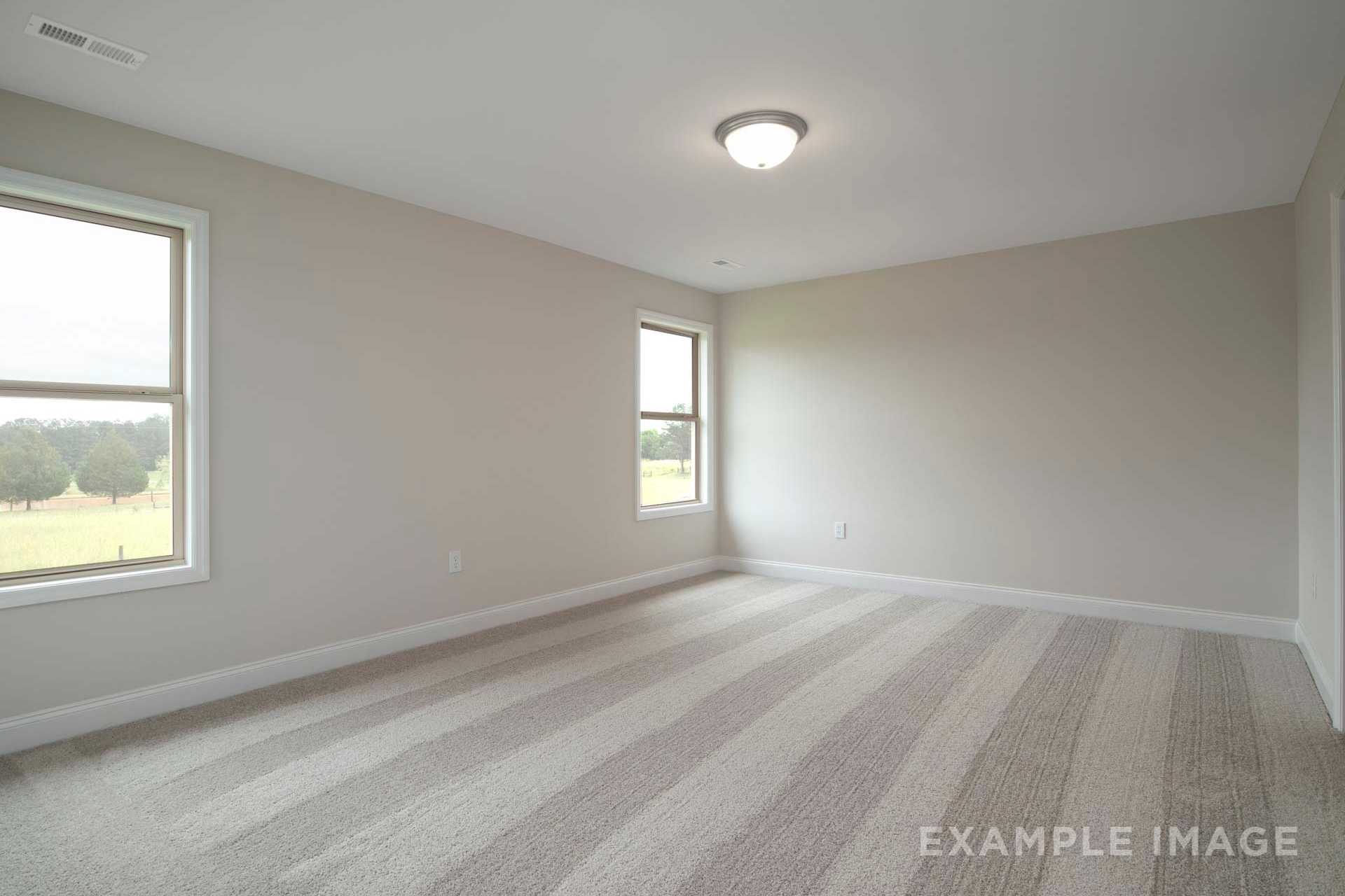 Spacious empty bedroom in The Charleston D showcasing neutral beige walls, large windows with field views, and striped carpet flooring