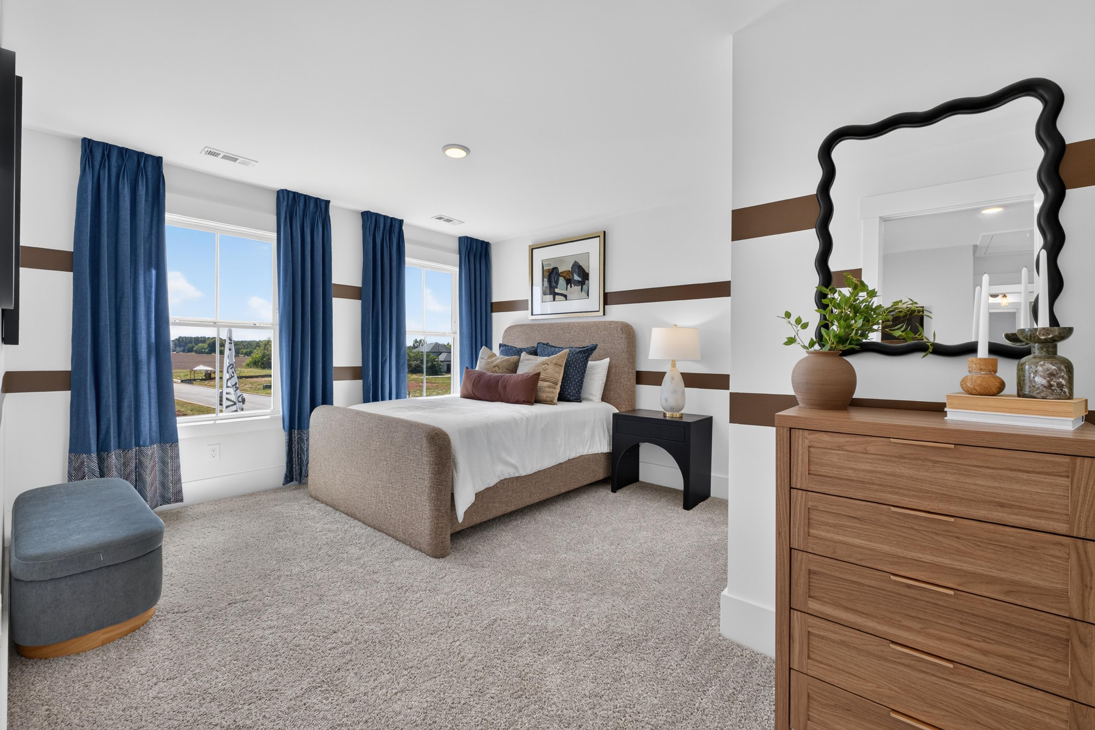 Primary bedroom at Evergreen Mill in Madison, Alabama by Davidson Homes with upholstered bed, wood dresser, and blue curtains