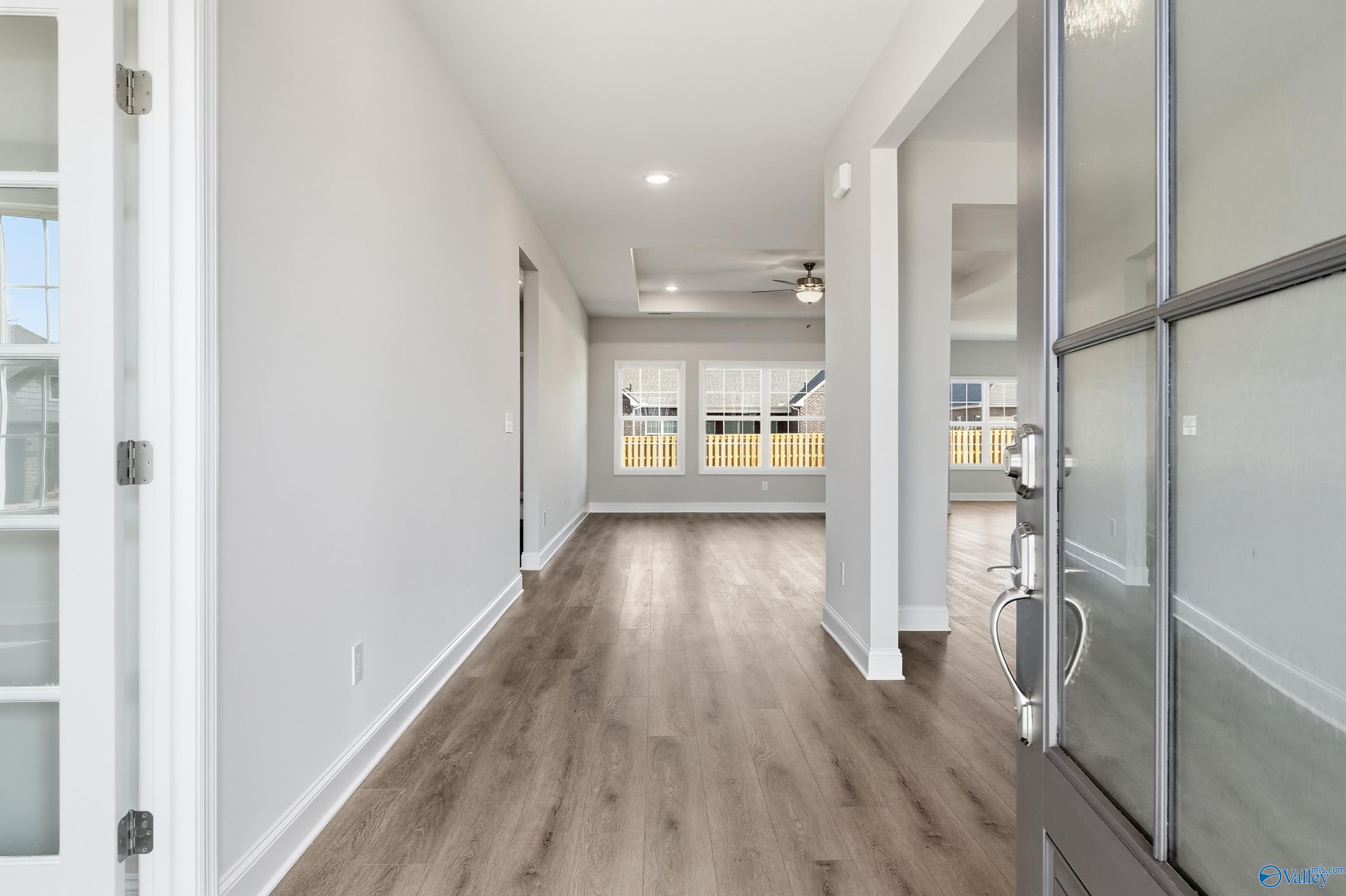 Bright entry hallway with hardwood floors, white walls, ceiling fan, and glass doors in Davidson Homes The Finleigh, Harvest, Alabama
