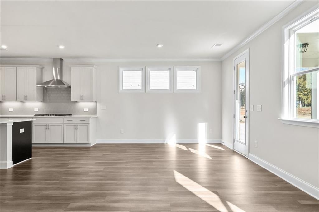 Spacious open-concept kitchen with white cabinets, stainless steel appliances, island, and hardwood floors in The Ash C at Wehunt Meadows, Hoschton