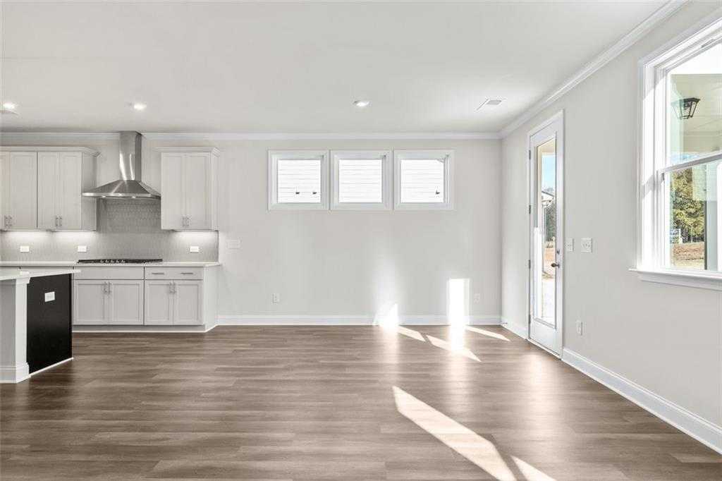 Spacious open-concept kitchen with white cabinets, stainless steel appliances, island, and hardwood floors in The Ash C at Wehunt Meadows, Hoschton