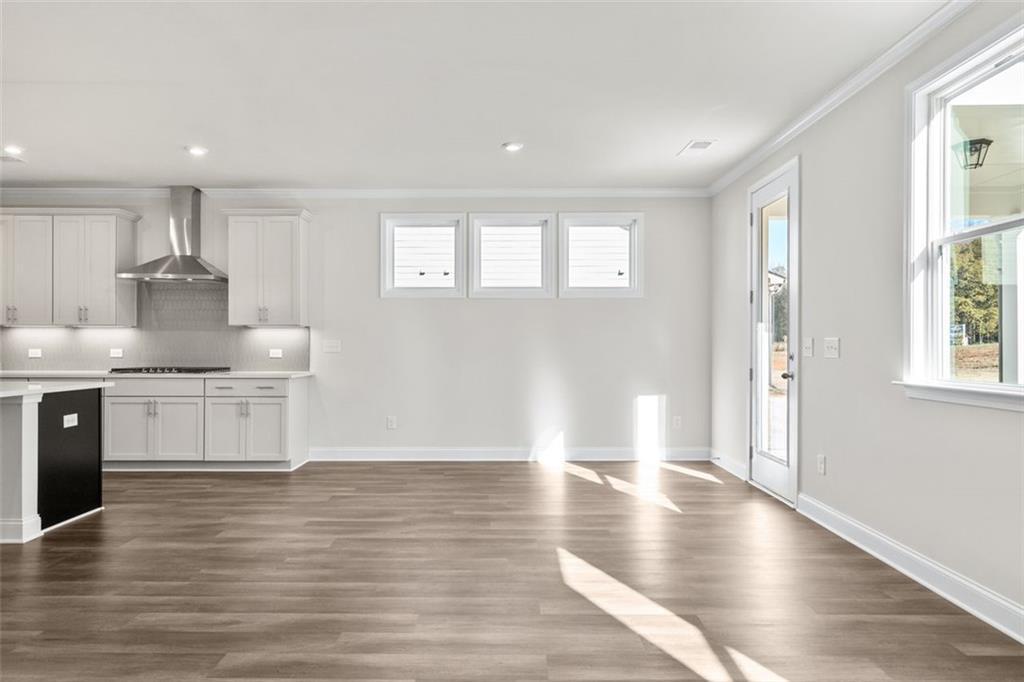 Spacious open-concept kitchen with white cabinets, stainless steel appliances, island, and hardwood floors in The Ash C at Wehunt Meadows, Hoschton