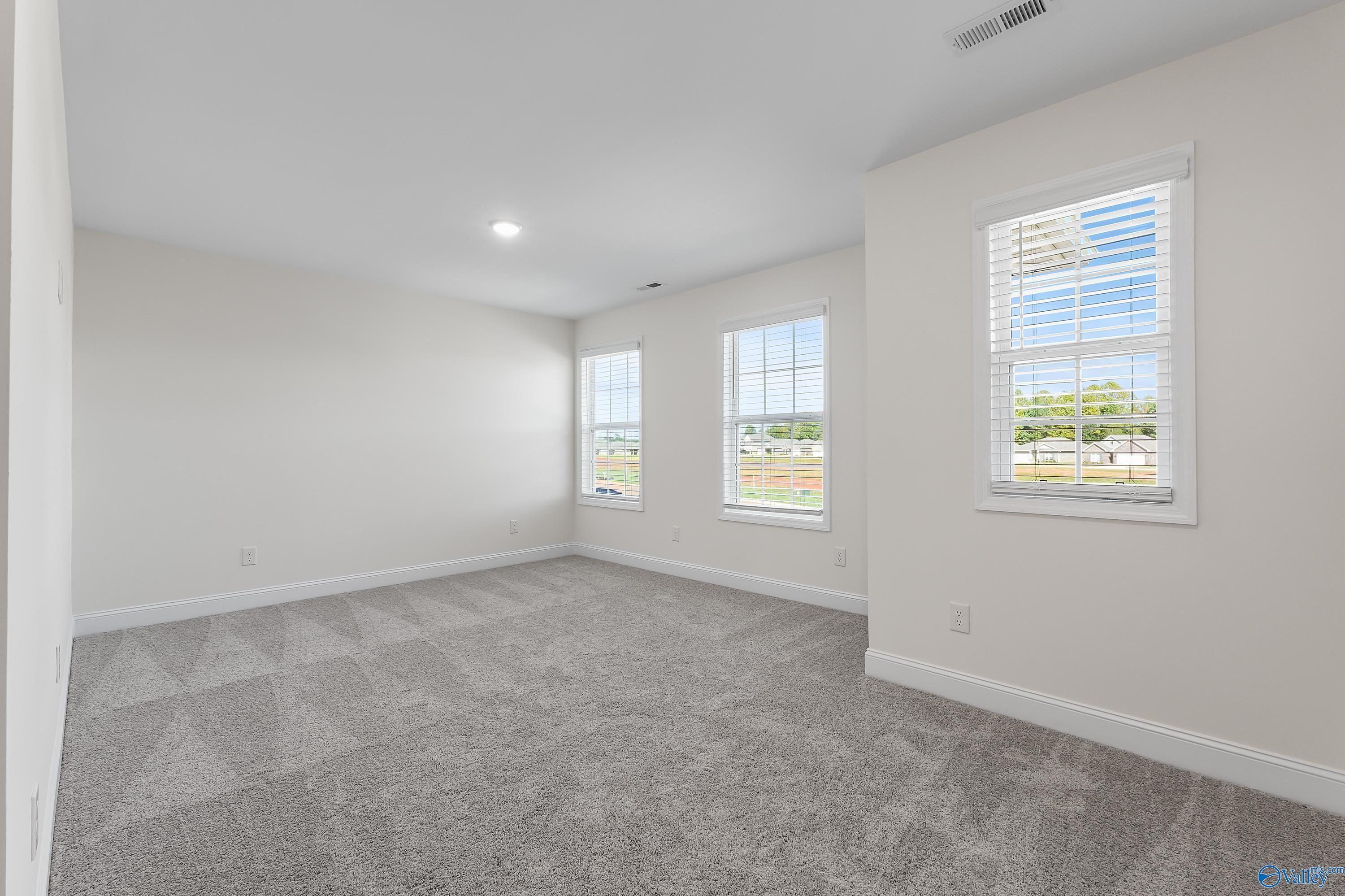 Bright empty bedroom with gray carpet, beige walls, and large windows in Davidson Homes The Shelby A, Athens AL