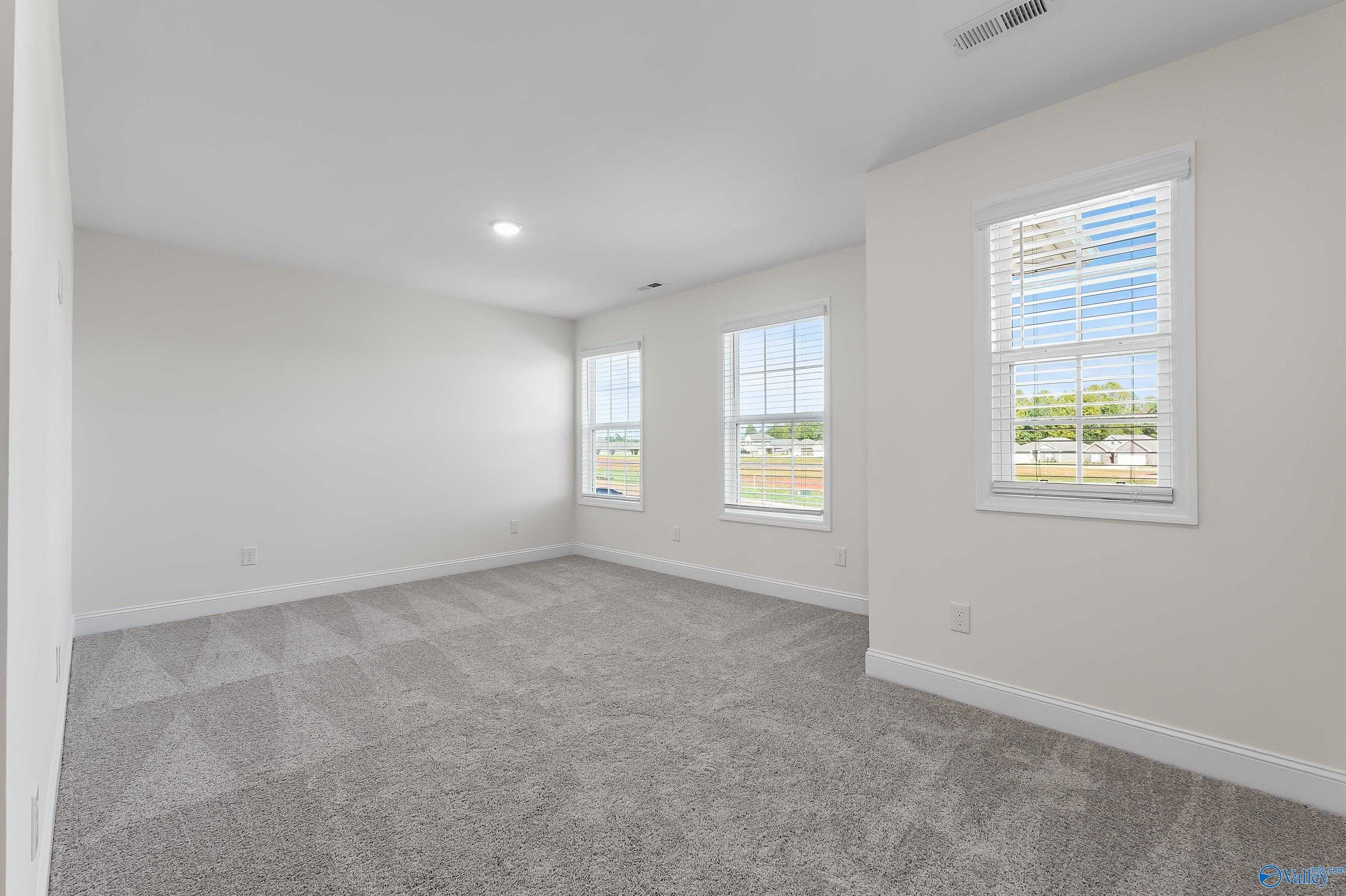 Spacious secondary bedroom with gray carpet, beige walls, and large windows in Davidson Homes The Shelby A, Athens, Alabama