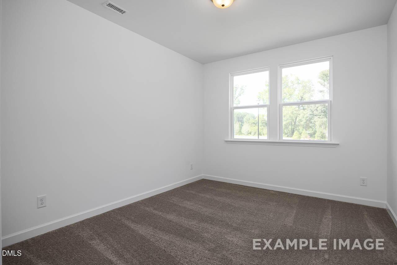 Bright bedroom with large double windows, white walls, and plush carpet in Davidson Homes The Willow D, Zebulon, NC