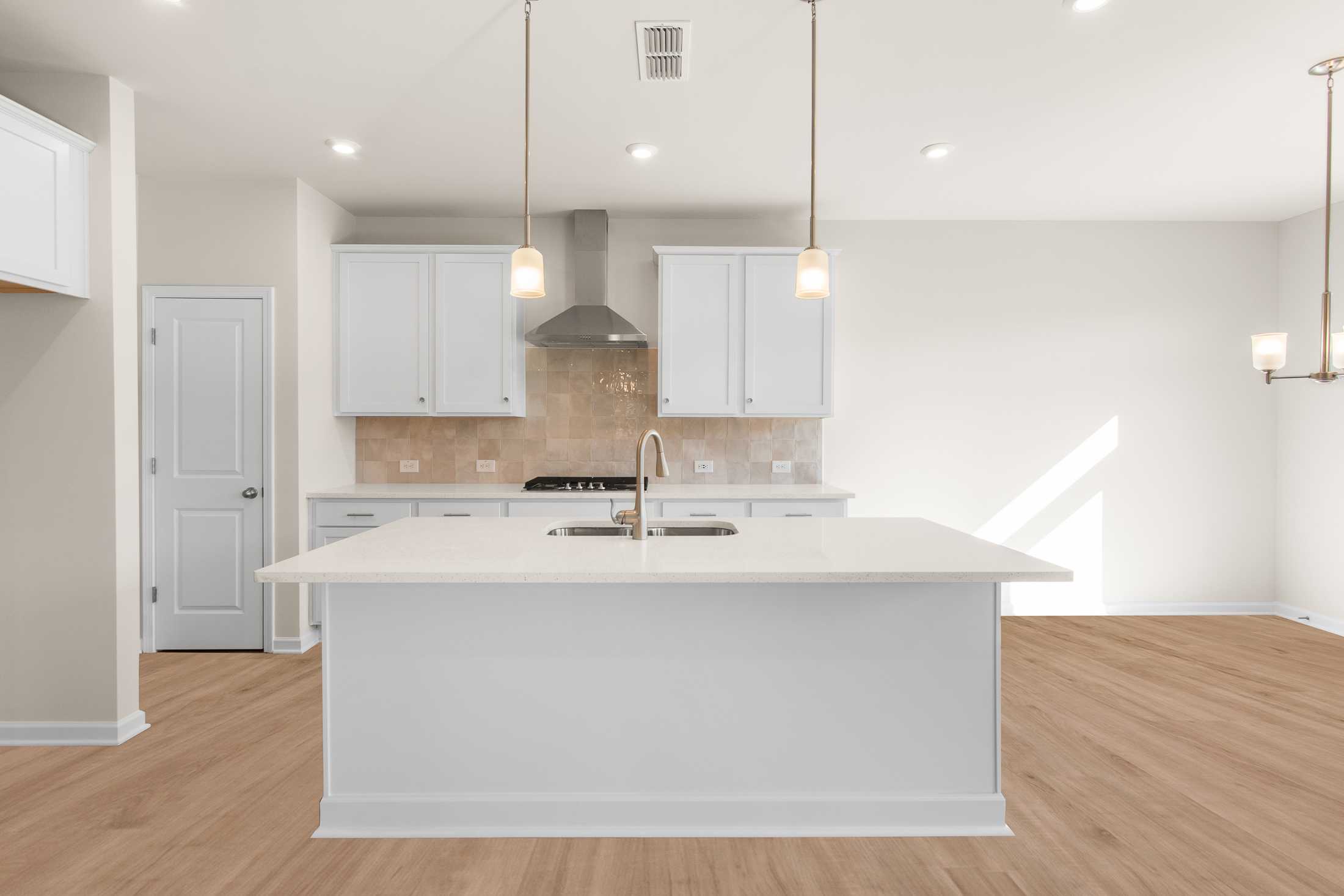 Spacious gourmet kitchen in The Willow B with white shaker cabinets, large quartz island sink, subway tile backsplash, and hardwood floors