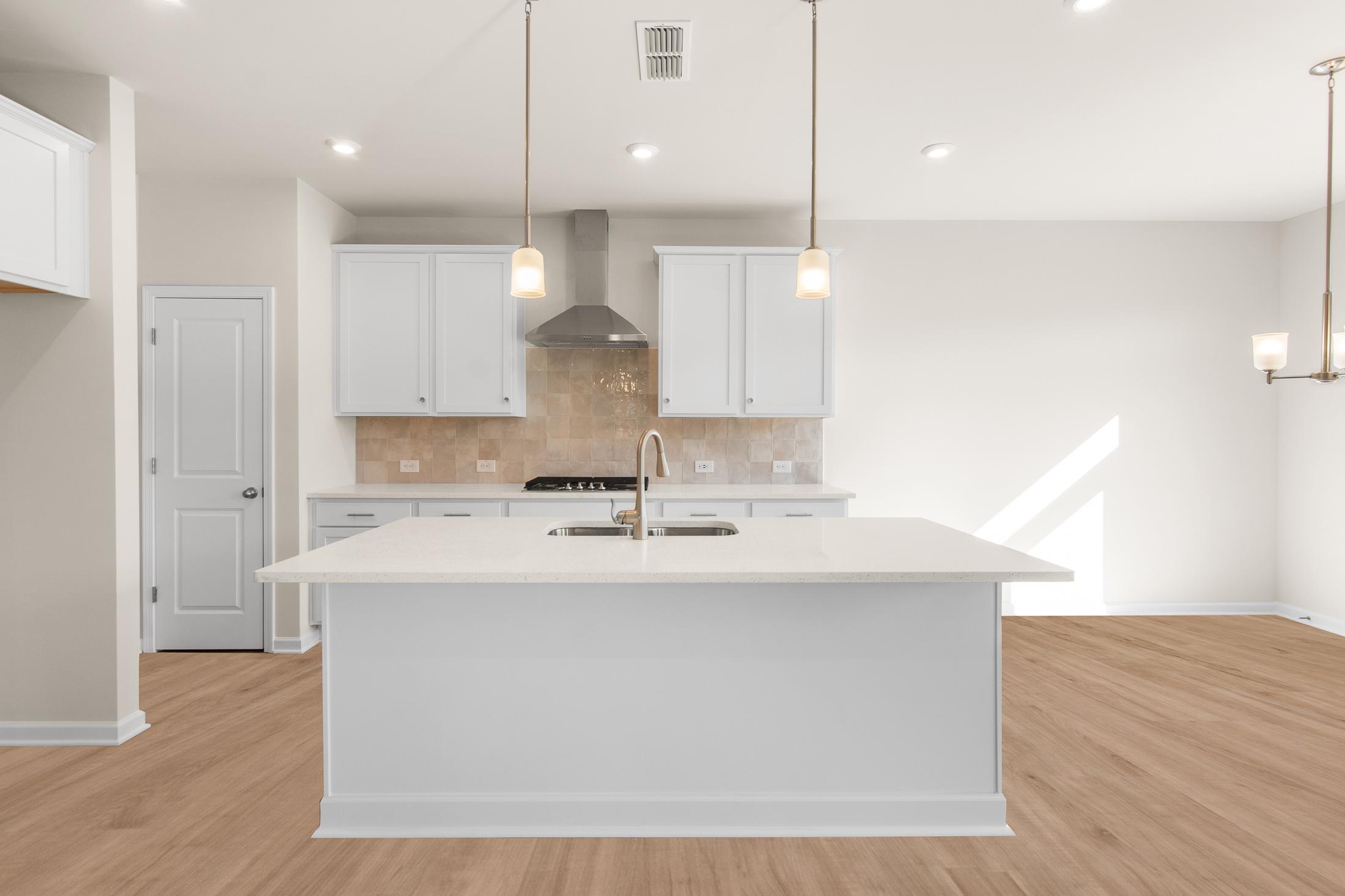 Spacious gourmet kitchen in The Willow B with white shaker cabinets, large quartz island sink, subway tile backsplash, and hardwood floors