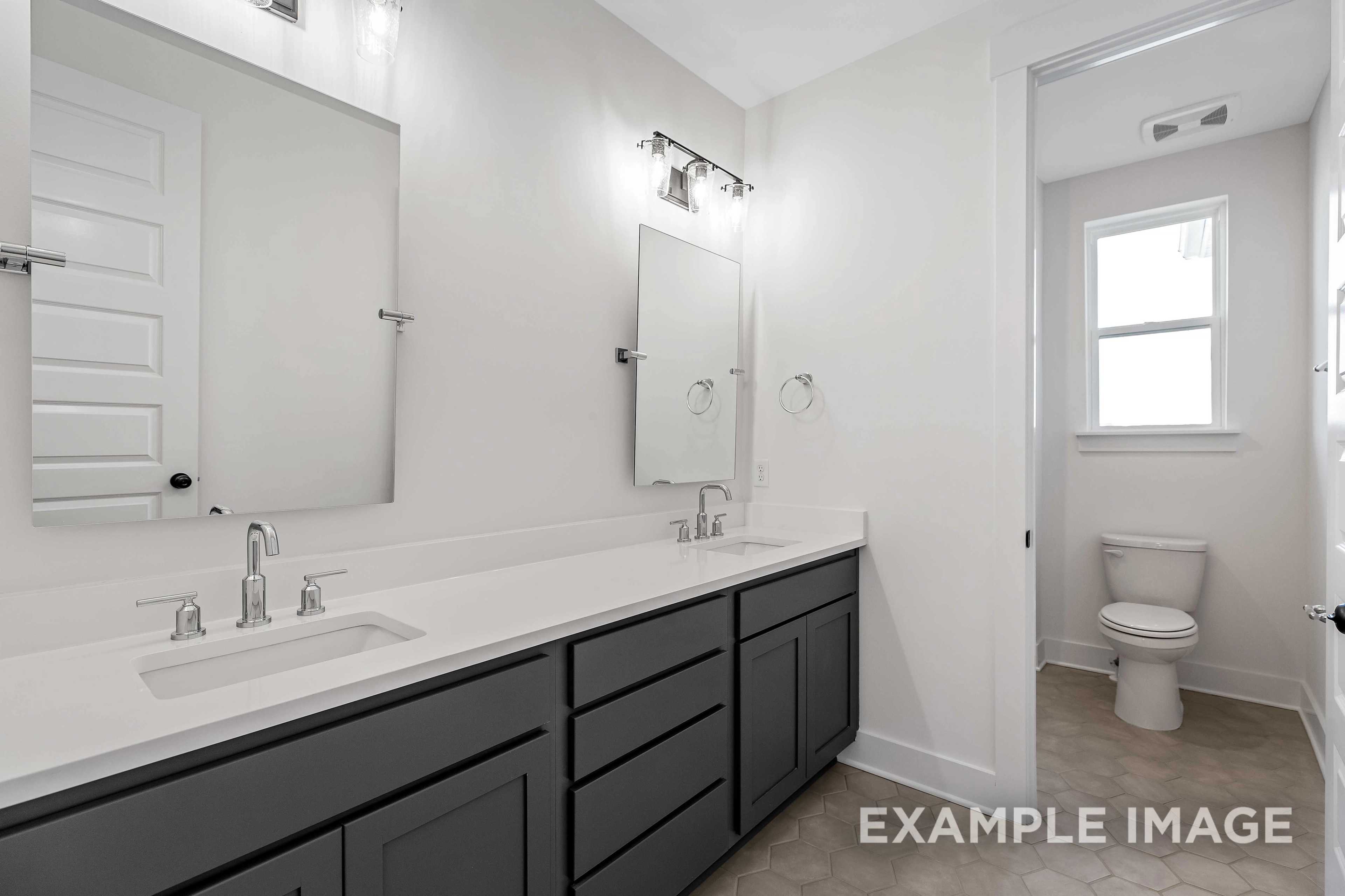 Spacious master bathroom in The Albany A featuring double vanity with gray cabinets, large mirror, and adjacent toilet