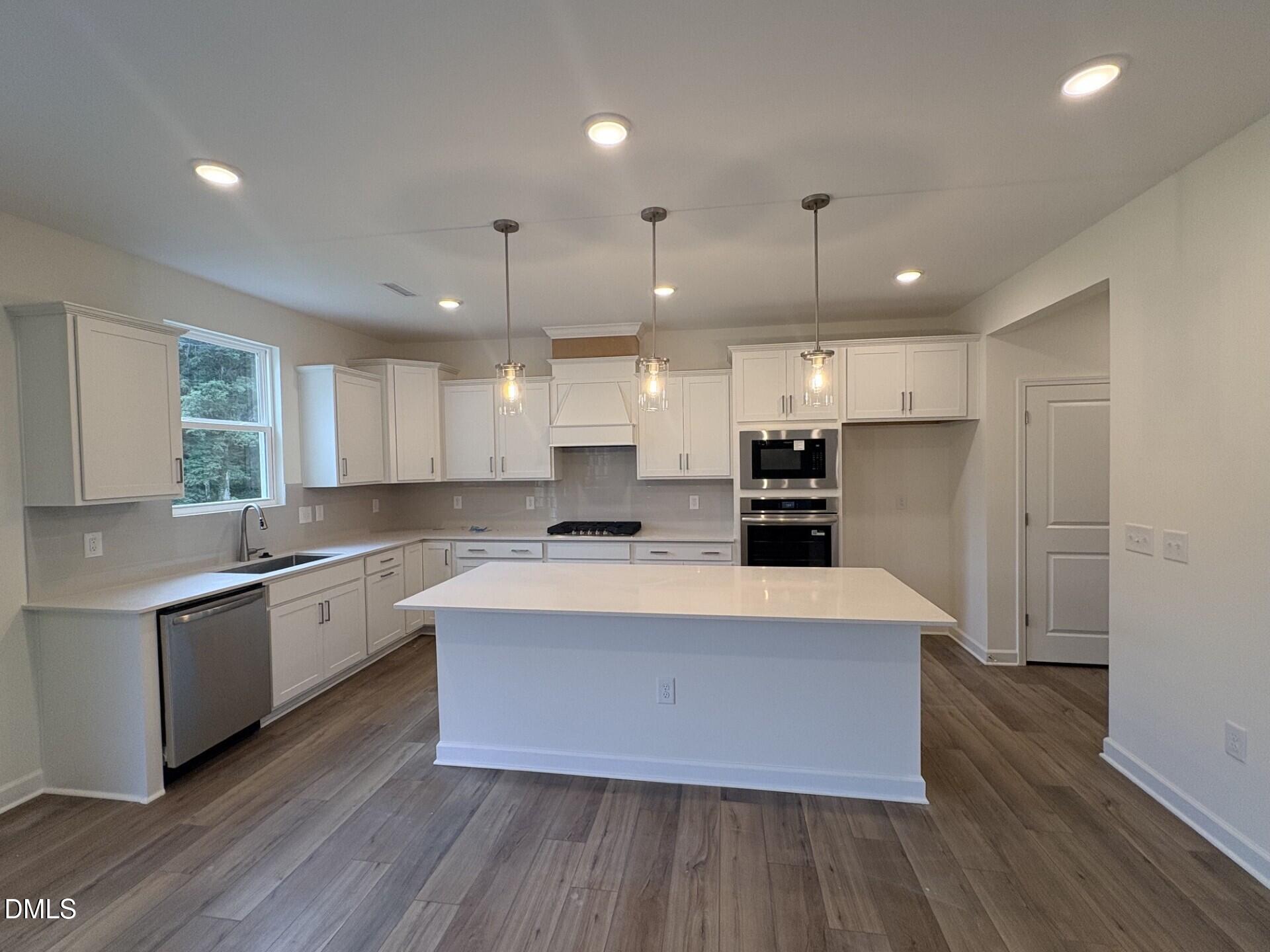 White kitchen with large island, pendant lights, stainless appliances, and wood-look floors in Davidson Homes Hickory II B, Zebulon NC
