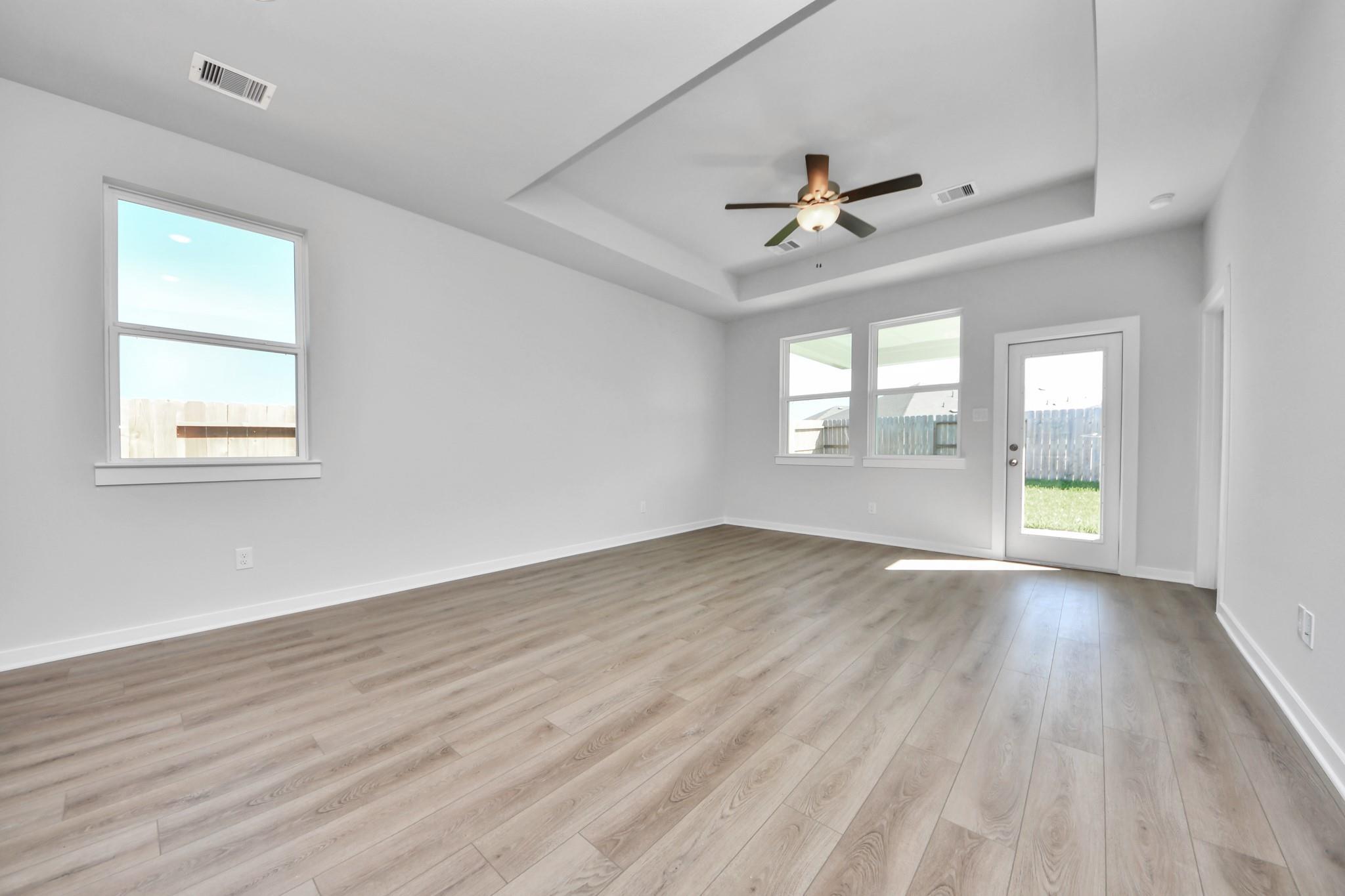 Spacious living area with tray ceiling, ceiling fan, and luxury vinyl plank flooring in The Colorado G home in Emberly.
