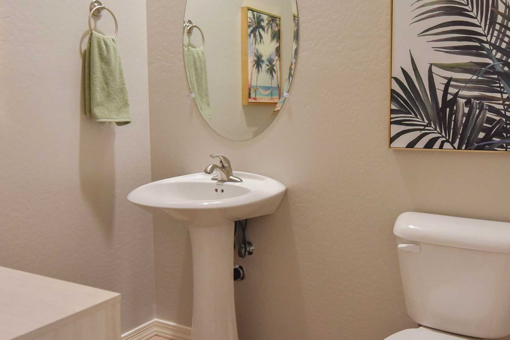 The Harmony master bathroom featuring white pedestal sink, toilet, round mirror, tropical palm art, and green towels