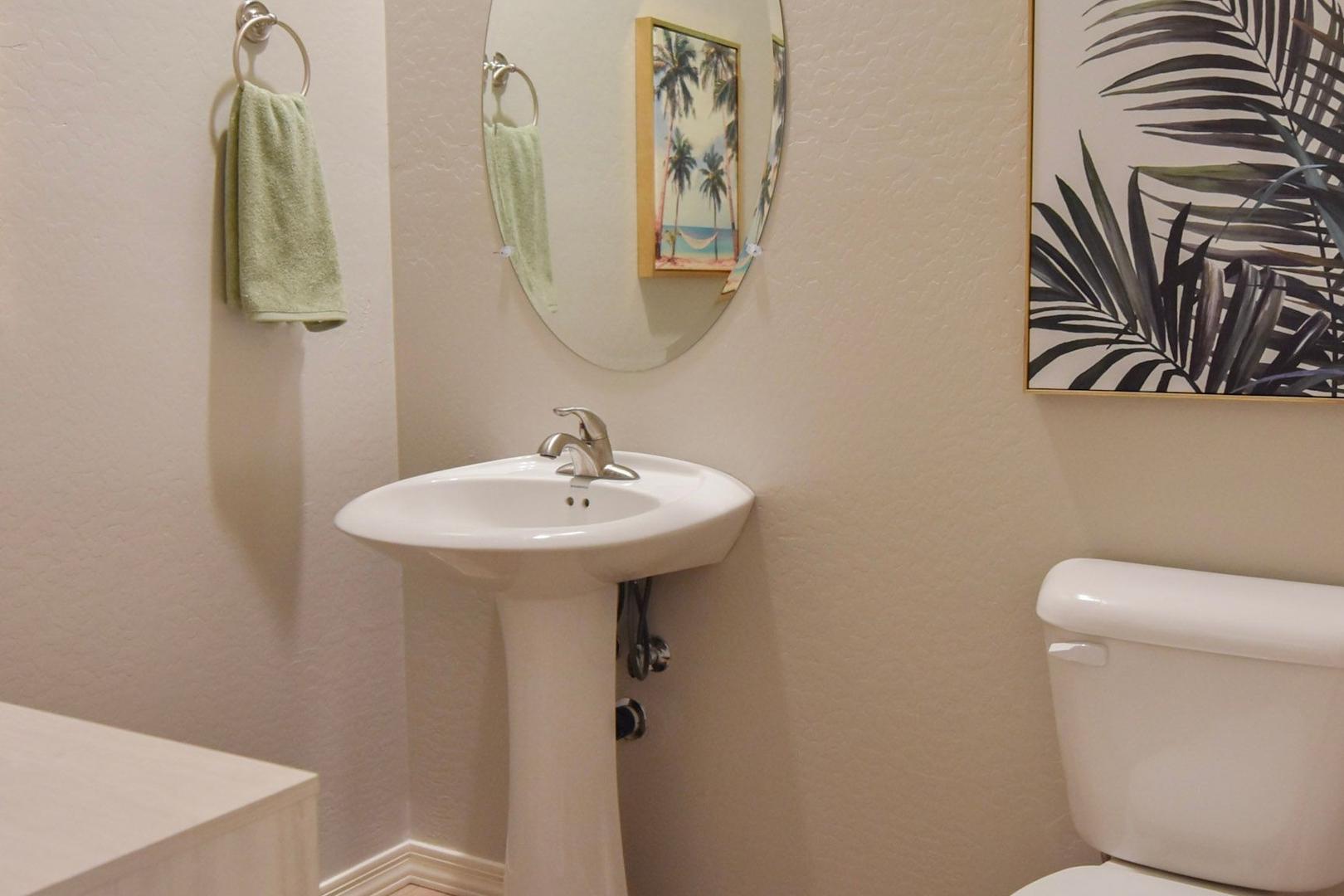 Master bathroom in The Harmony B by Davidson Homes: white pedestal sink, toilet, tropical palm art, round mirror, green towels