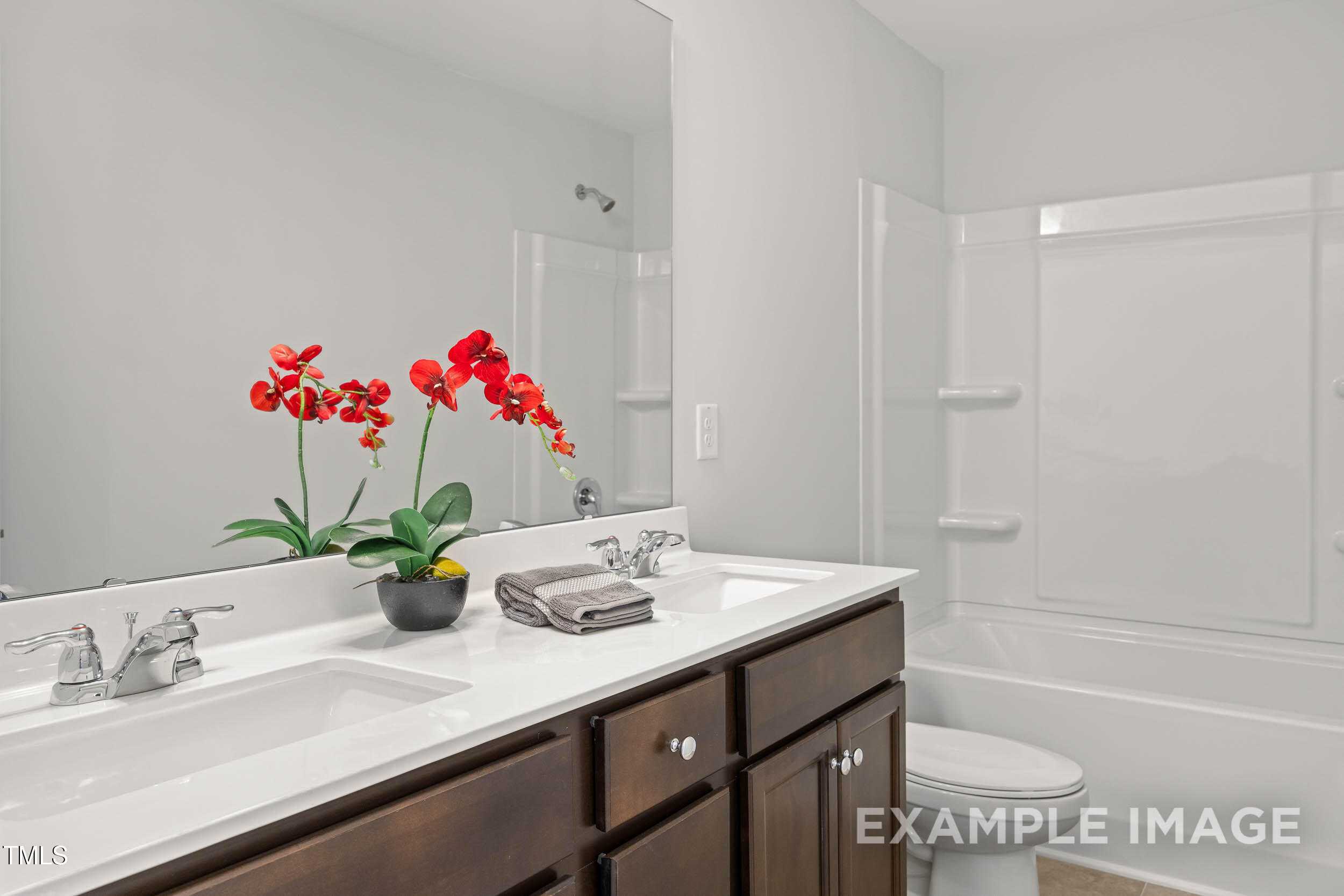 Elegant double vanity bathroom with dark wood cabinets, white tub-shower, orchids in Davidson Homes The Graham Interior, Fuquay-Varina, NC