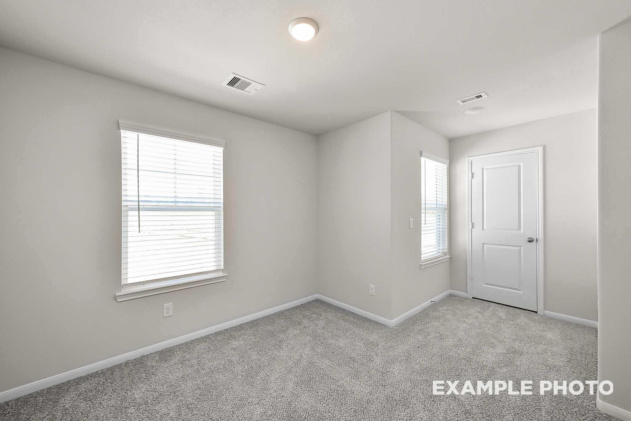 Bright secondary bedroom with plush carpet and windows in The Blanco F floor plan at Spring Branch Crossing, Conroe, Texas.