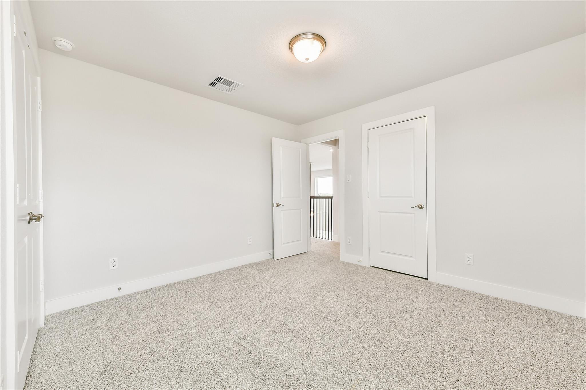 Spacious empty upstairs bedroom with white walls, beige carpet, and open door to balcony railing in Davidson Homes The Victoria A, Texas City