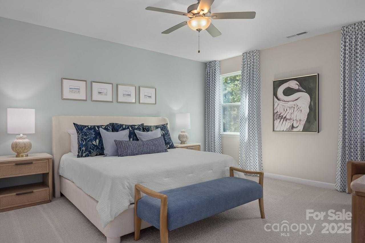Elegant master bedroom with light blue walls, king bed, ceiling fan, swan artwork in Davidson Homes The Hickory E II, Belmont, NC