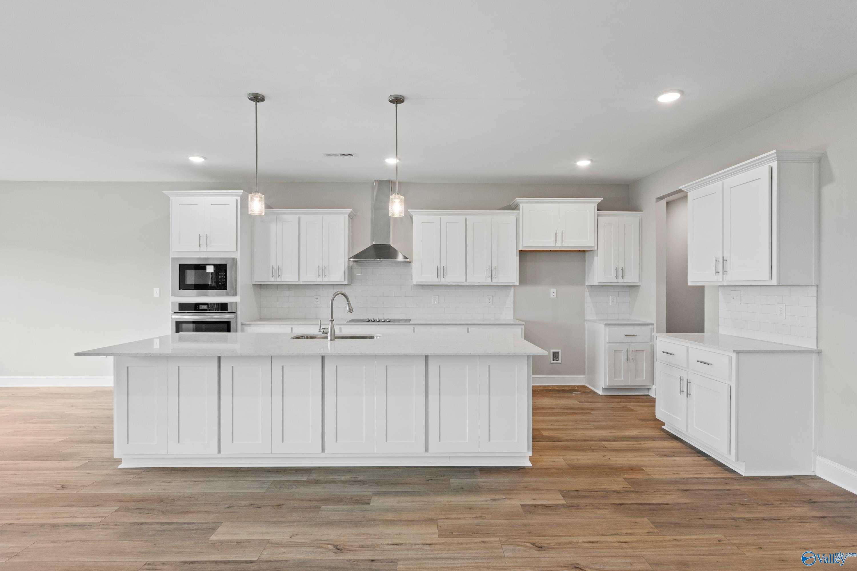 Modern white kitchen island with sink, stainless appliances, and hardwood floors in Davidson Homes The Finleigh, Meridianville, Alabama