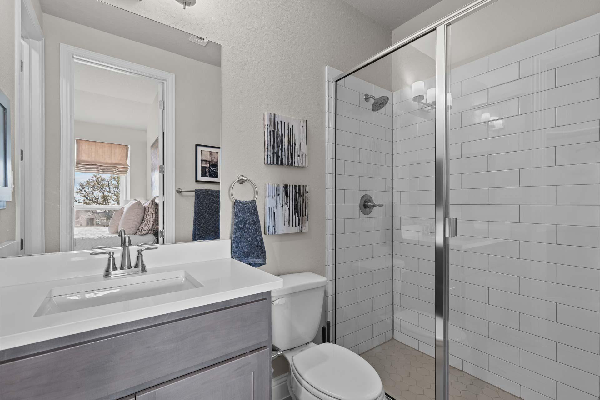 Spacious master bathroom in The Garner A with white subway tile walk-in shower, modern gray vanity, large mirror, and neutral tones