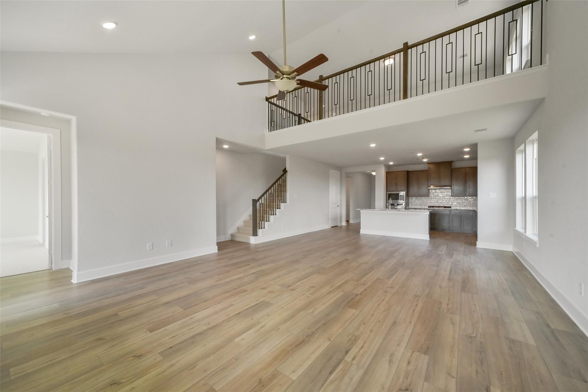 Spacious two-story living area with loft balcony, hardwood floors, and open kitchen in Davidson Homes The Zion A, Lago Mar, Texas City