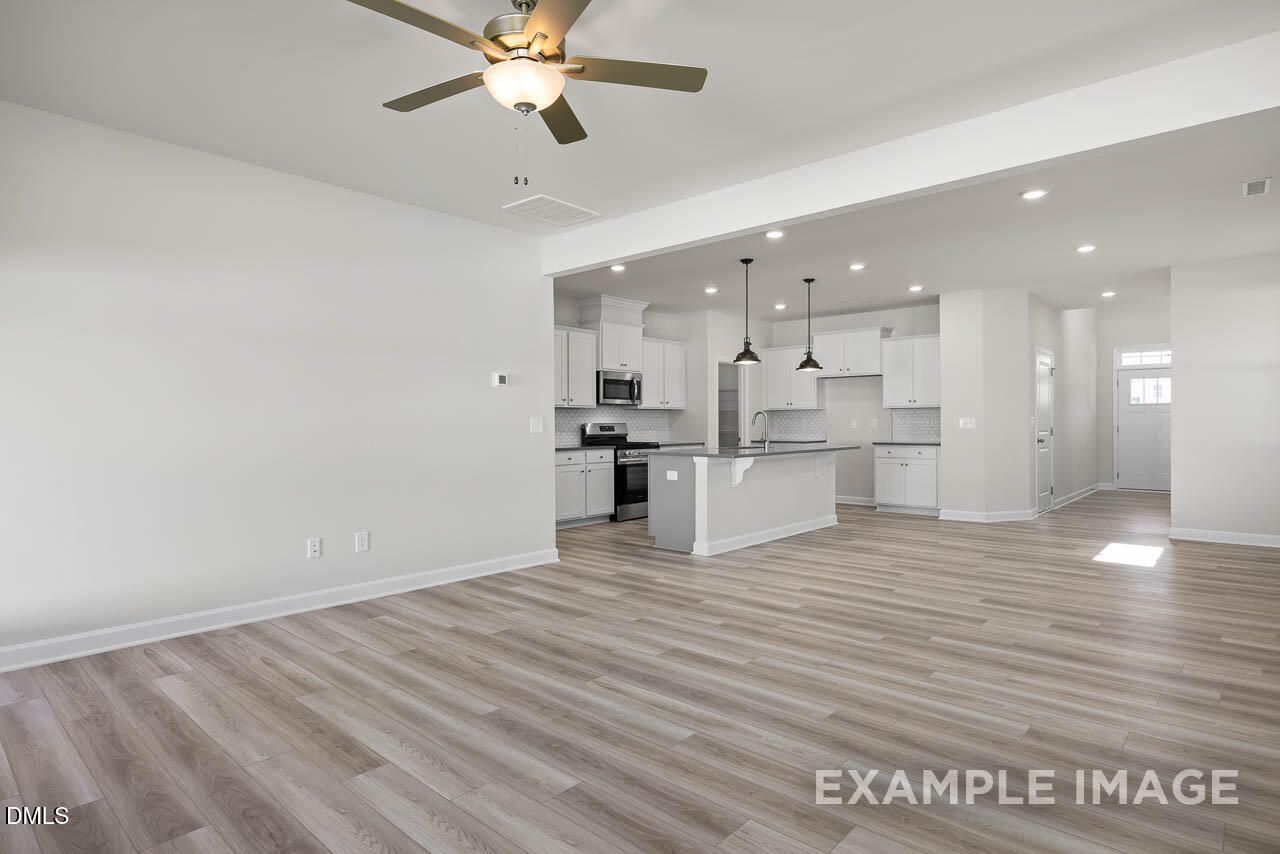 Open-concept kitchen with white cabinets, peninsula island, stainless appliances, and light wood floors in Davidson Homes The Adalynn A, Lillington, NC