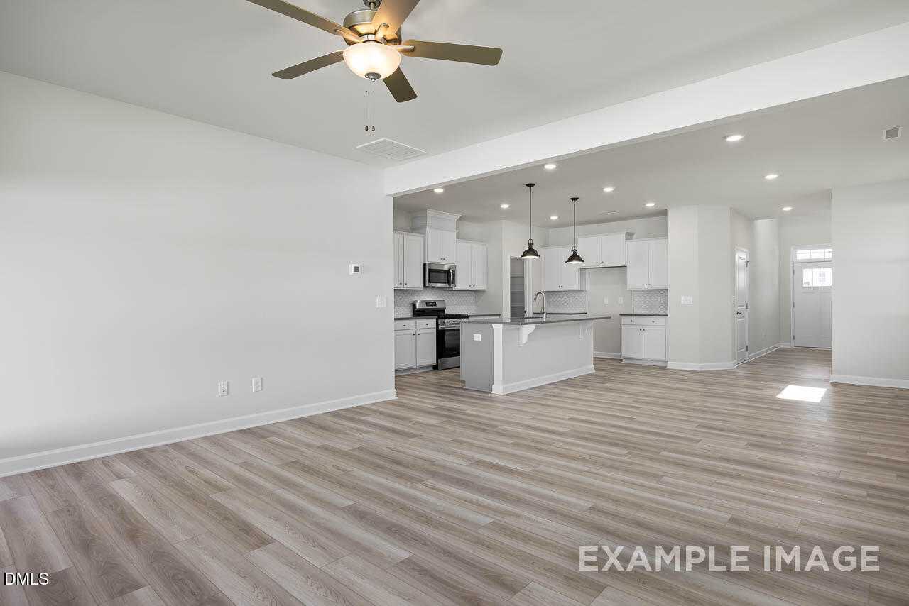 Open-concept kitchen with white cabinets, peninsula island, stainless appliances, and light wood floors in Davidson Homes The Adalynn A, Lillington, NC