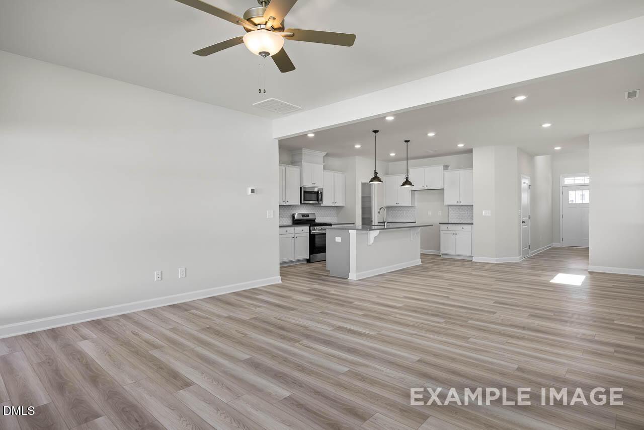 Modern open-concept kitchen with white shaker cabinets, stainless appliances, island, and ceiling fan in The Adalynn A by Davidson Homes, Lillington NC