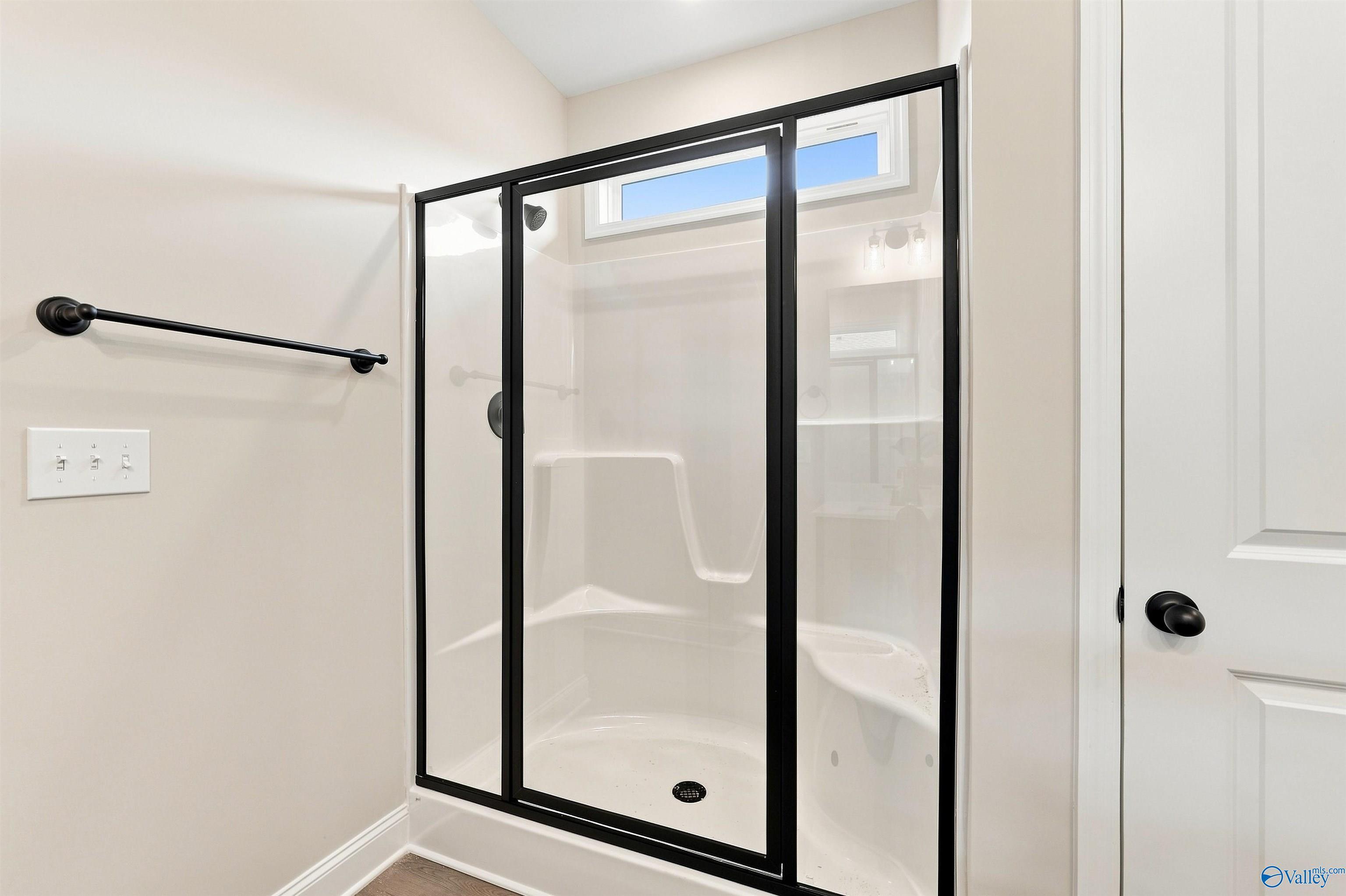 Modern glass-enclosed shower with black hardware in bathroom of Davidson Homes Franklin C plan, The Meadows, Athens, Alabama