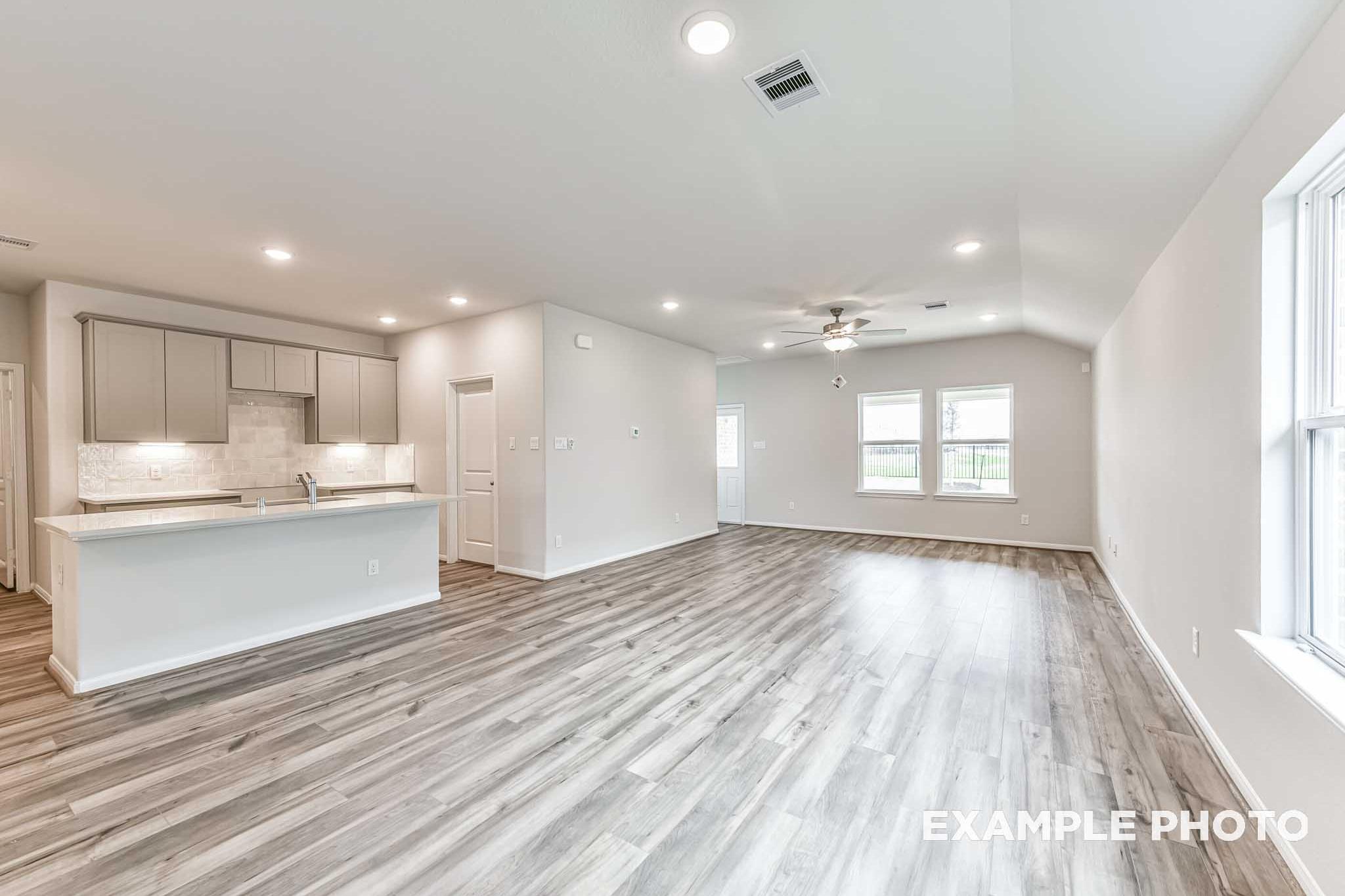 Spacious open-concept kitchen in The Laguna A with white shaker cabinets, large center island, hardwood floors, and living area