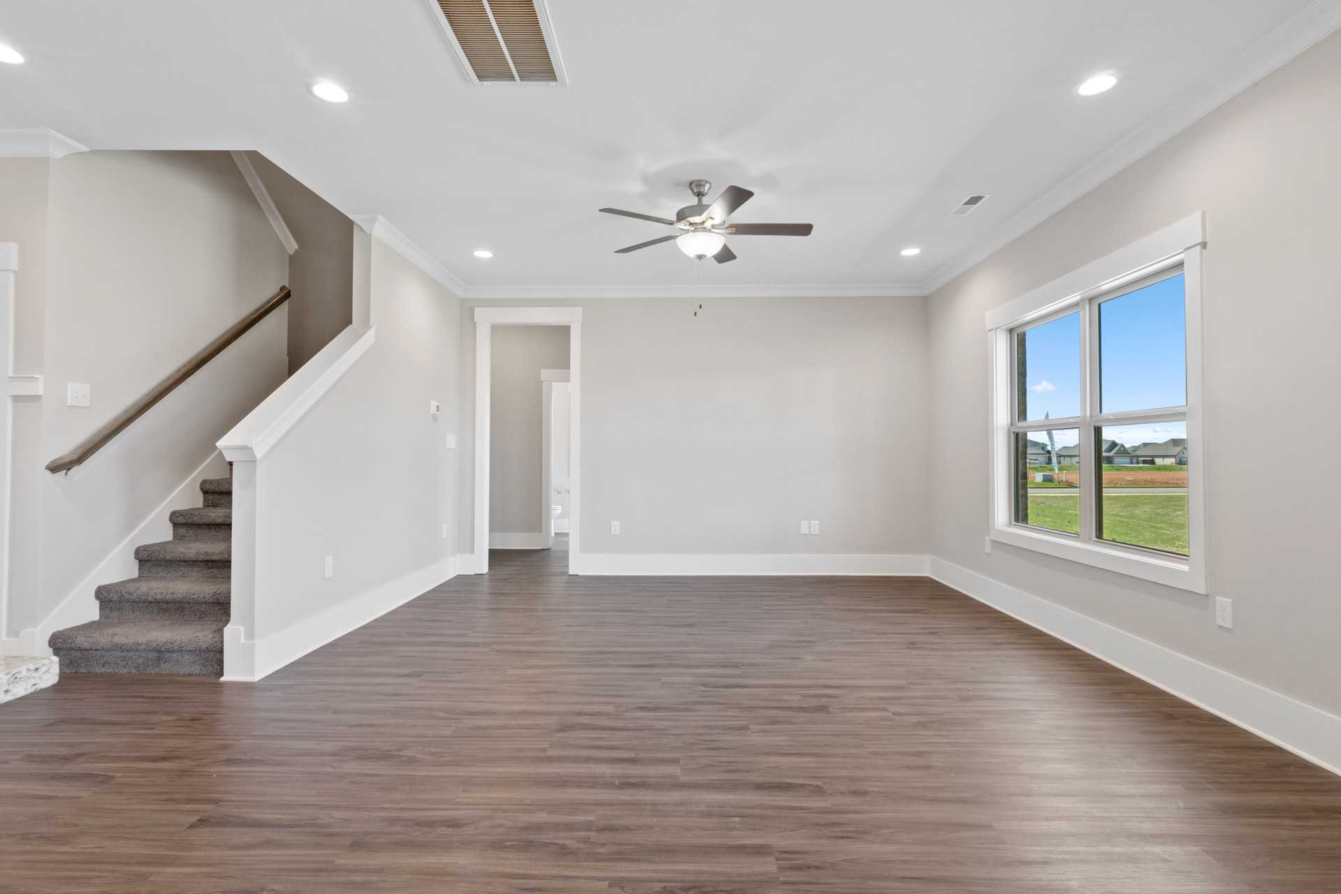 Spacious open-concept living room in Little Burwell Estates, Harvest Alabama featuring hardwood floors, ceiling fan, and large window with field view