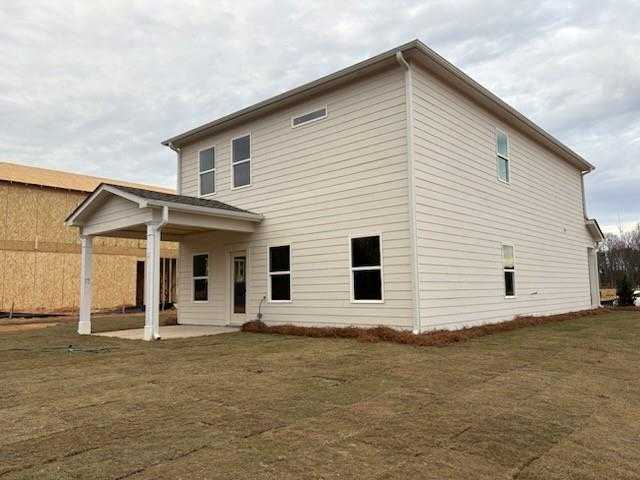 Two-story beige-sided Rabun C home by Davidson Homes in Cedar Farms, Winder, GA, featuring covered front porch, garage, and grassy yard