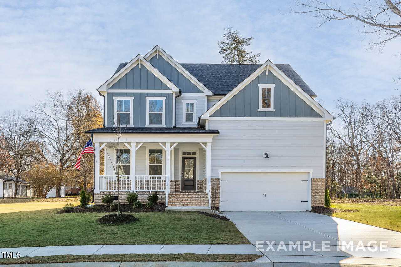 Blue and white Craftsman-style 4-bedroom home with gabled roof, covered porch, American flag, and 2-car garage in Retreat at North Main, Lillington, NC