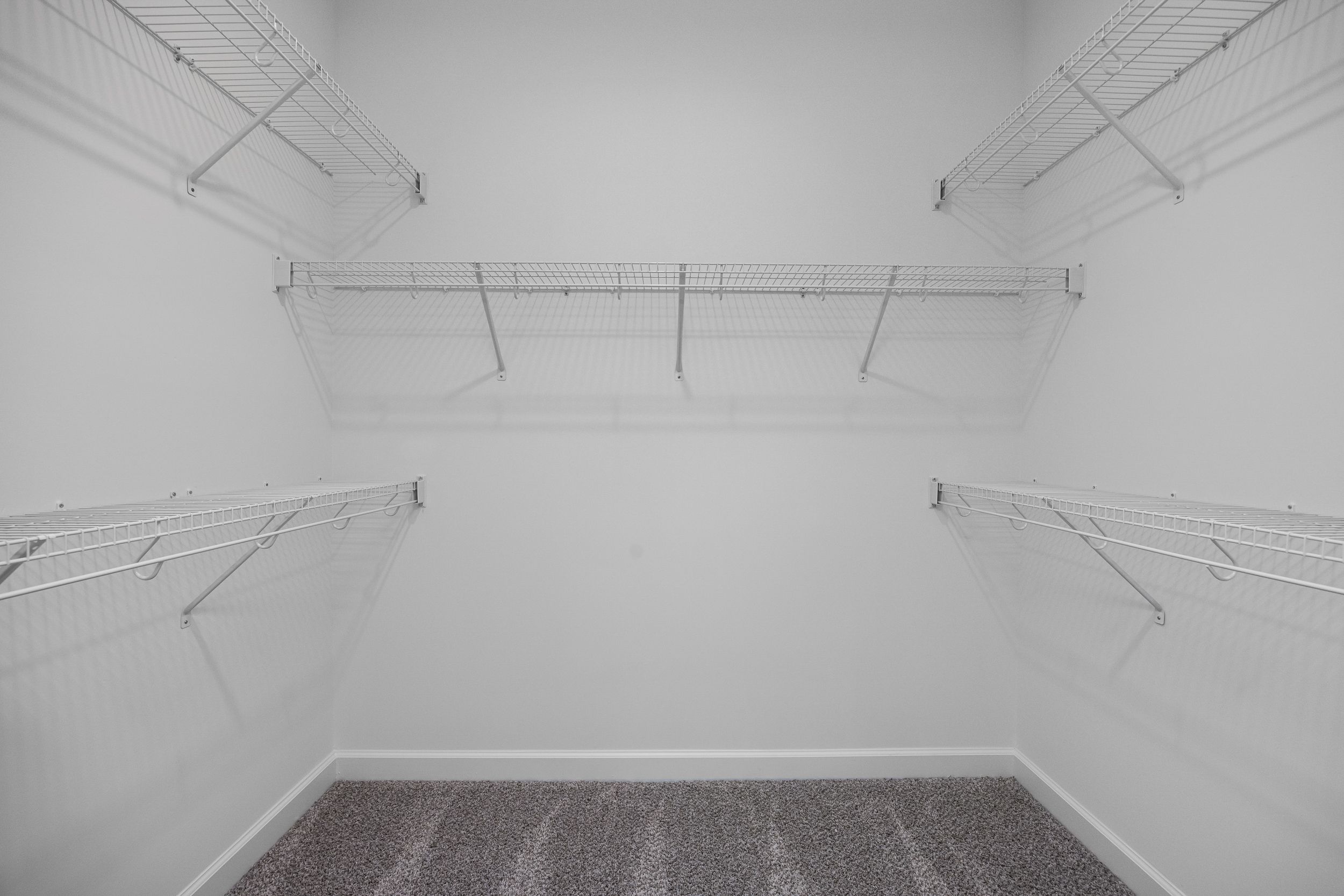 Spacious walk-in master closet in The Magnolia B with white wire shelving on three walls and light carpet floor