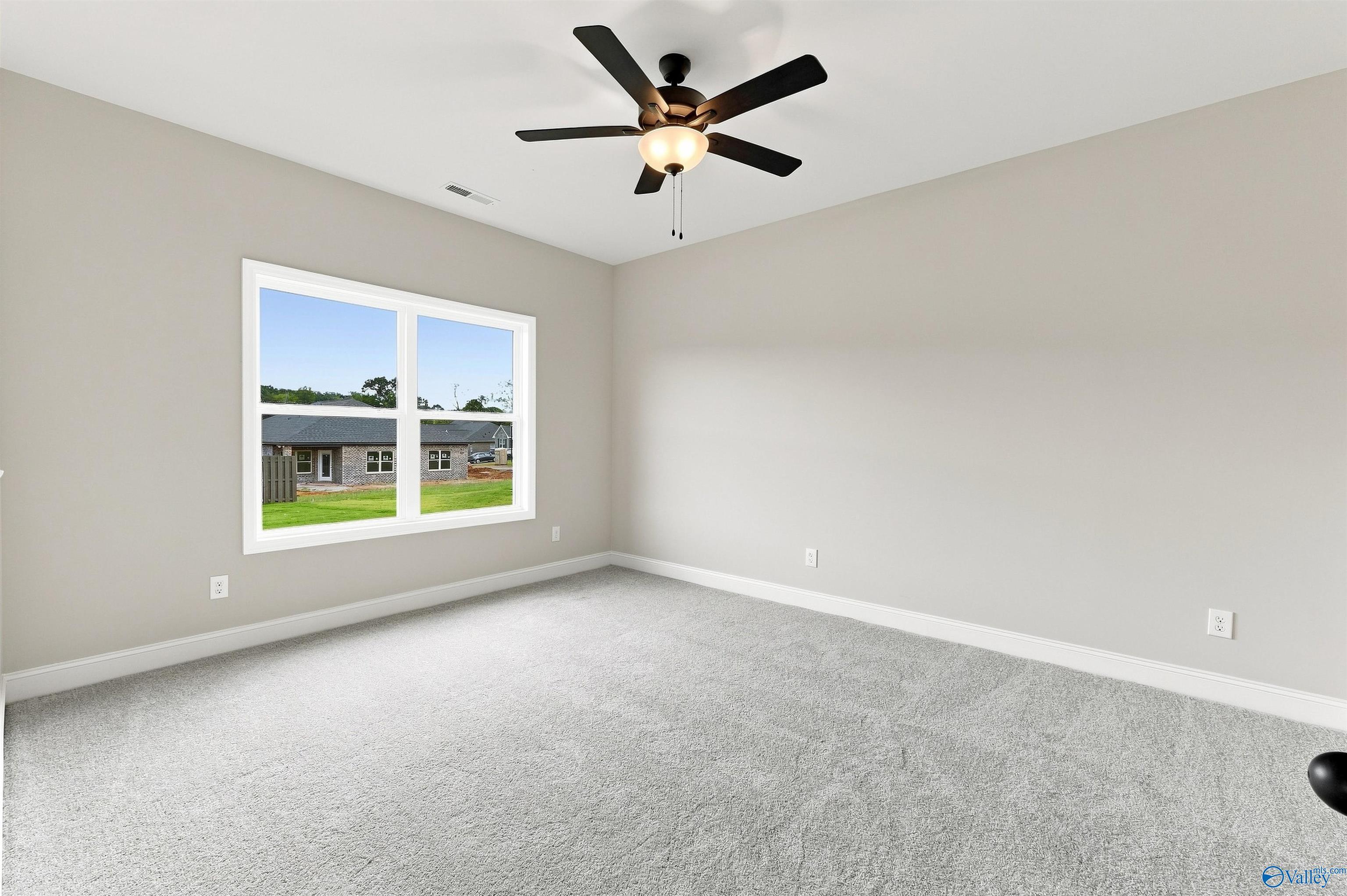 Bright bedroom with gray carpet, ceiling fan, and window view in Davidson Homes Franklin C plan, The Meadows, Athens, Alabama