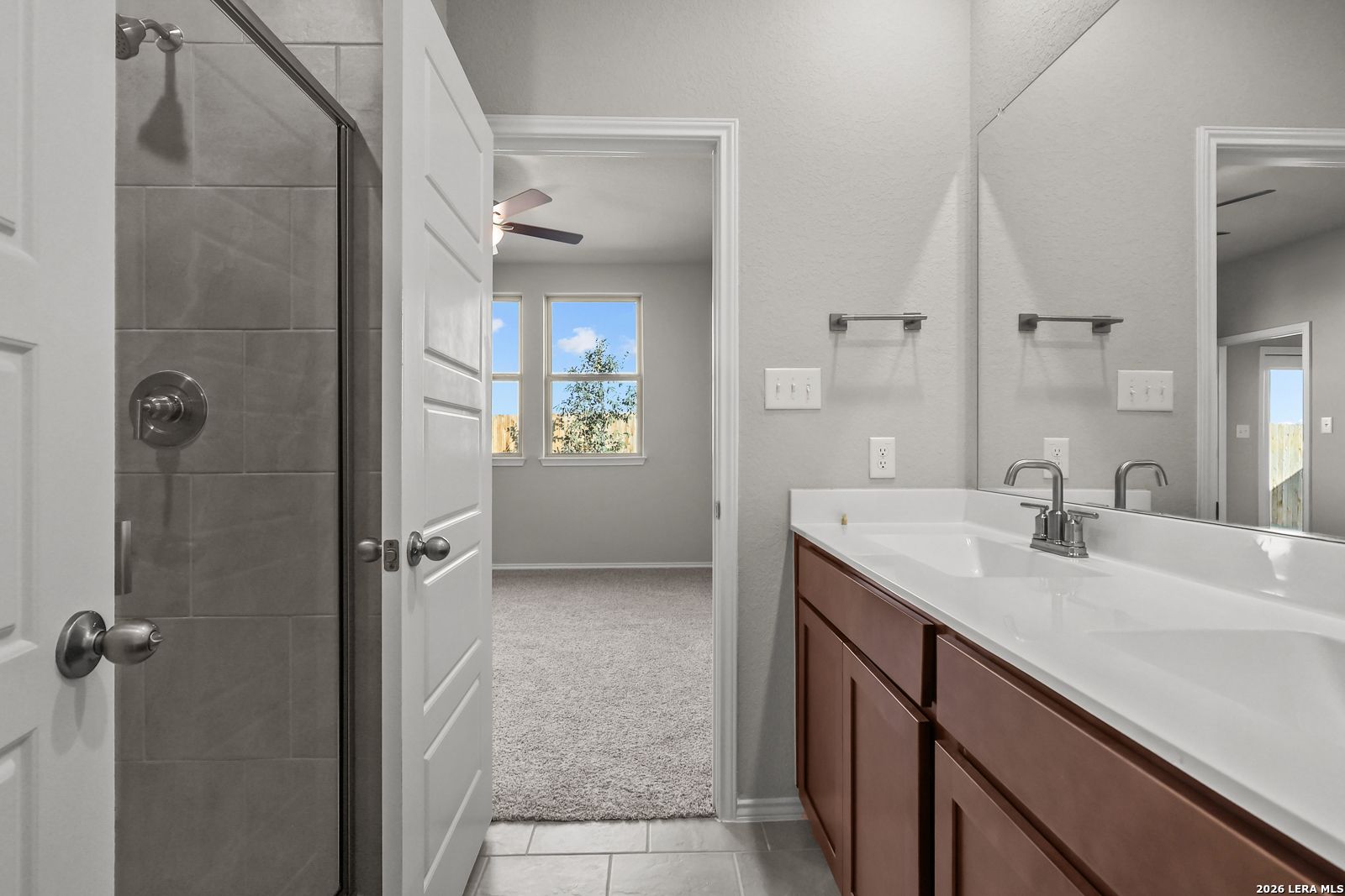 Modern master bathroom featuring walk-in shower, double vanity, large mirror, and adjacent bedroom in Davidson Homes The Frio B, San Antonio