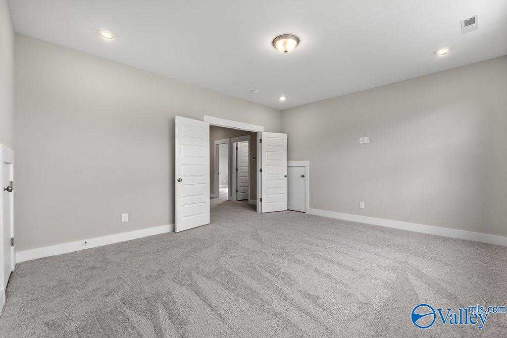 Spacious empty bedroom with gray carpet, light walls, open double doors to hallway, recessed lighting in Evermore Homes The Oxford, Owens Cross Roads, Alabama