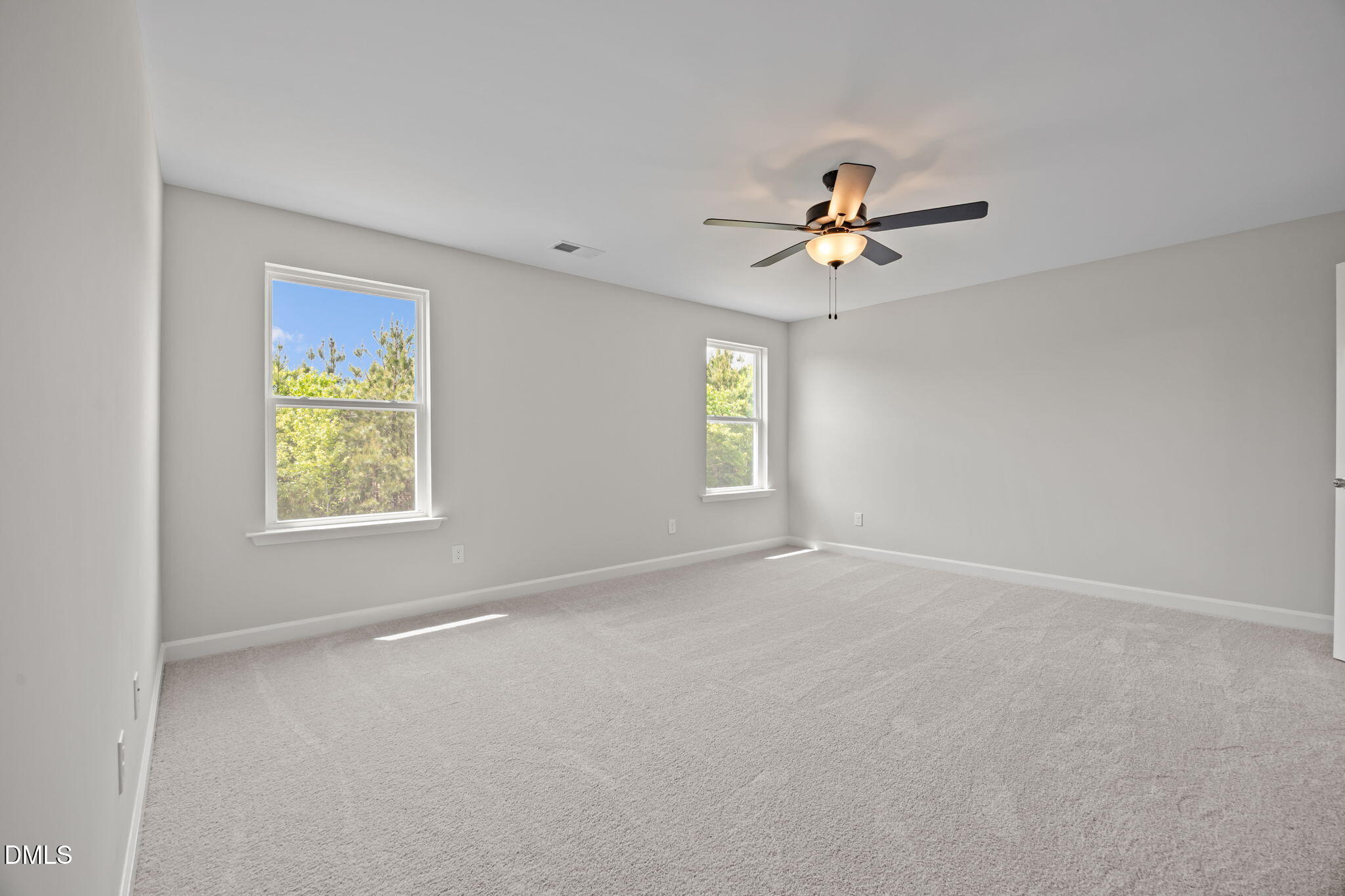 Bright secondary bedroom with light gray walls, beige carpet, ceiling fan, and tree-view windows in The Willow D, Wendell, NC