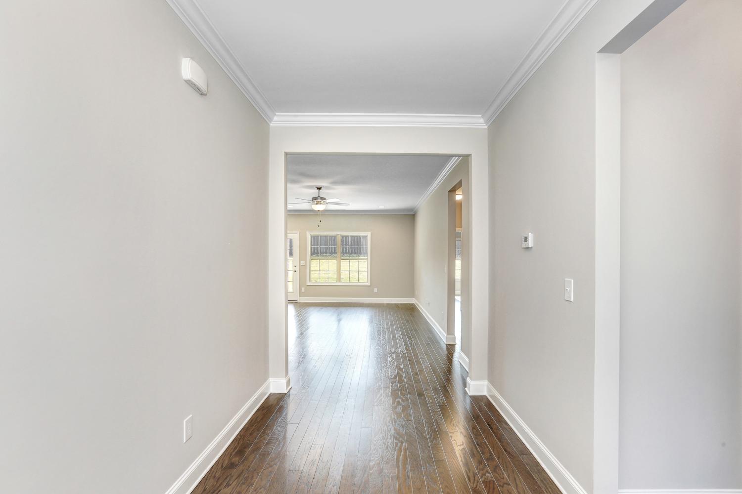 Spacious hallway in The Montgomery home with light gray walls, dark hardwood floors, ceiling fan, and open view to sunlit living area