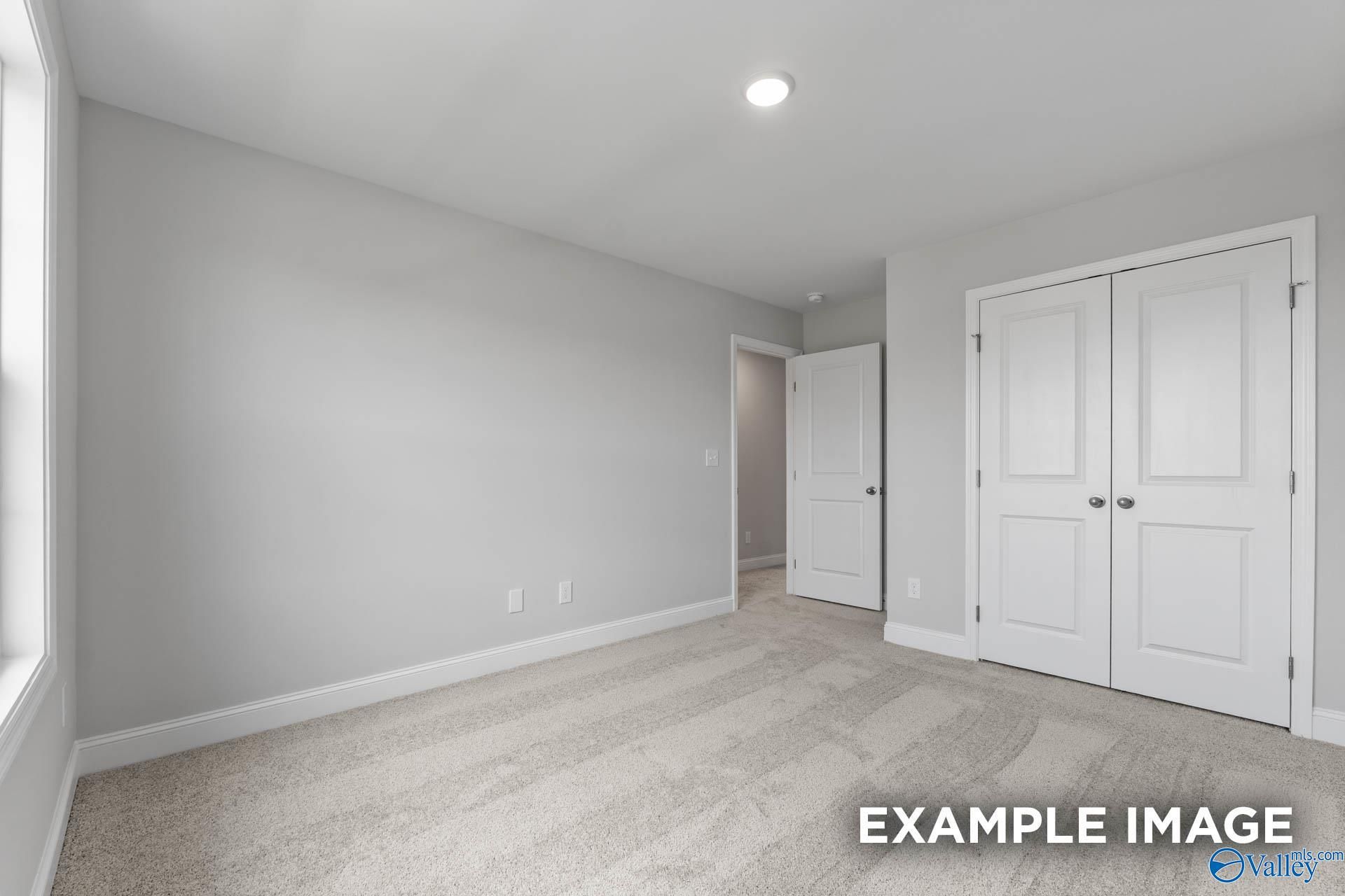 Spacious bedroom with light gray walls, plush carpet, double closet doors, and window in Evermore Homes The Madison D, Madison AL
