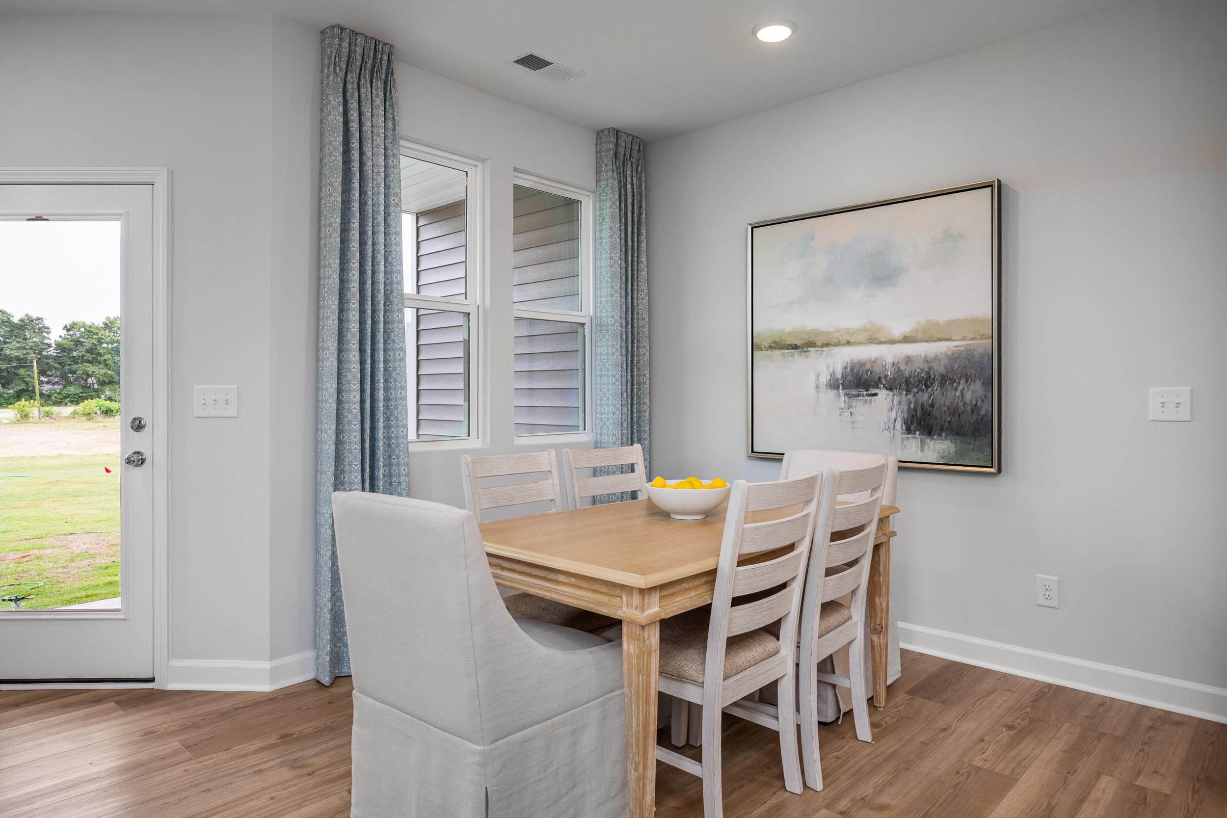 Bright dining room at Springvale in Fuquay-Varina NC with wooden table, skirted white chairs, orange bowl, and abstract painting