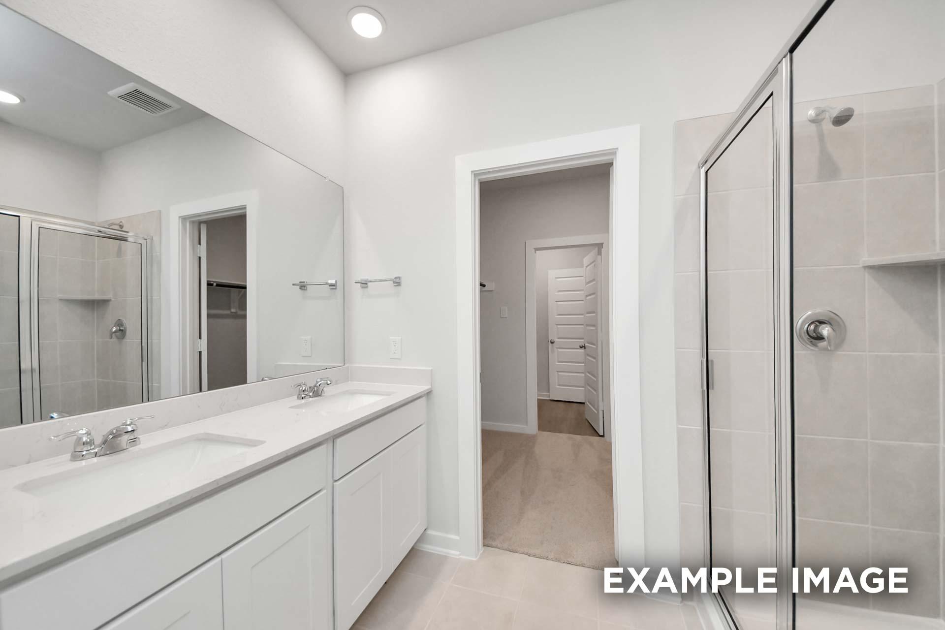 Spacious master bathroom in The Blanco by Davidson Homes featuring dual vanities, glass shower, and large mirror