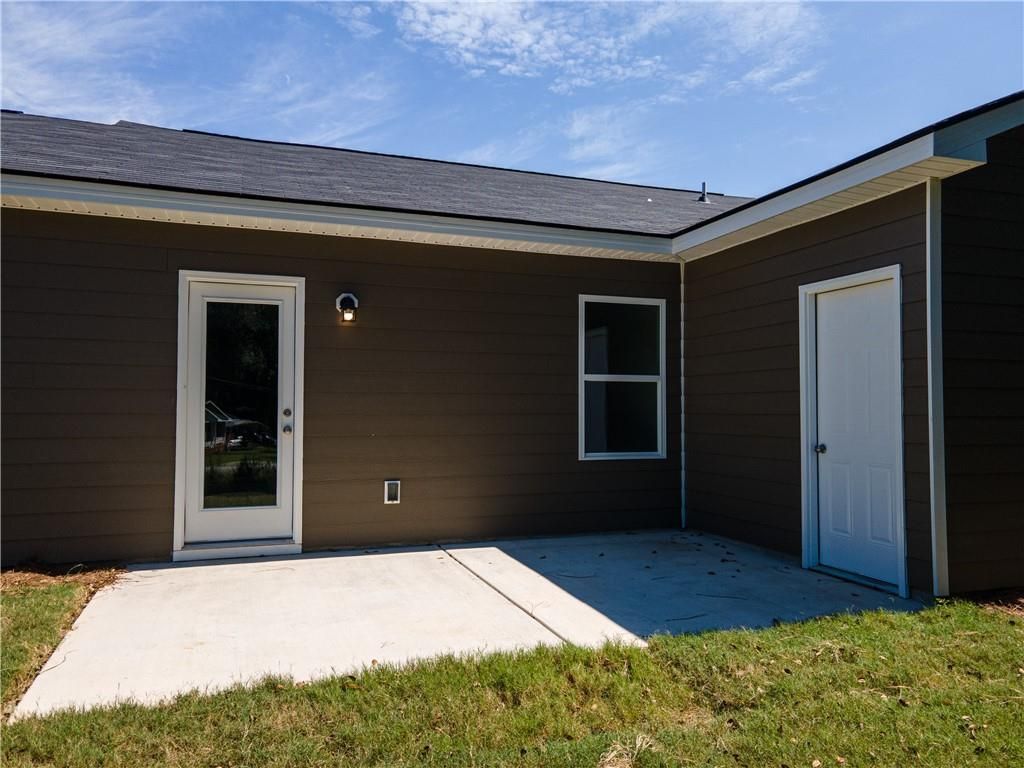 Brown-sided exterior of The Washington 3-bedroom home by Davidson Homes in Phenix City, Alabama, with white doors, window, and concrete patio on green lawn
