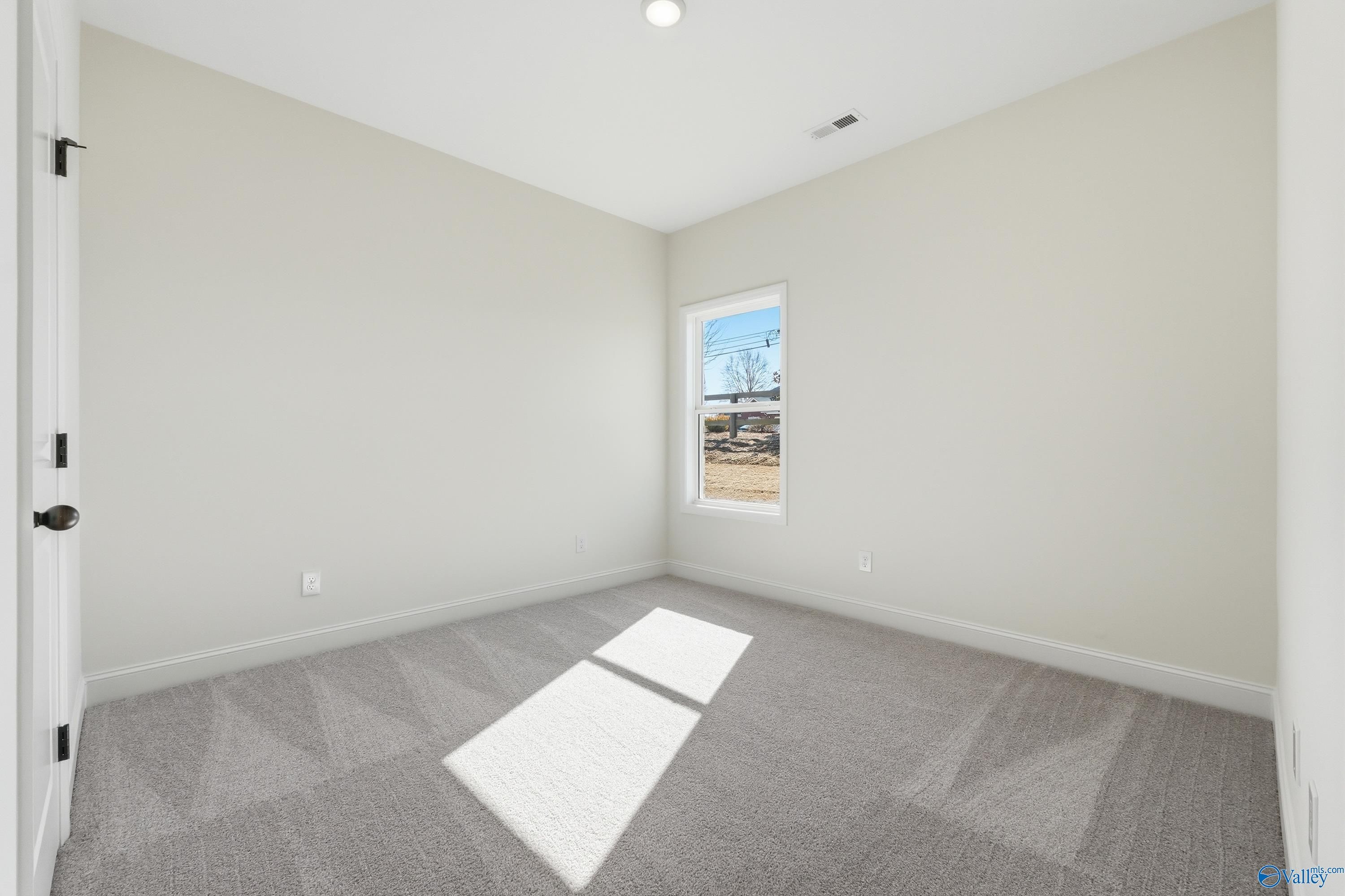 Bright secondary bedroom with beige walls, gray carpet, and sunlit window in Davidson Homes Franklin C, New Market, Alabama